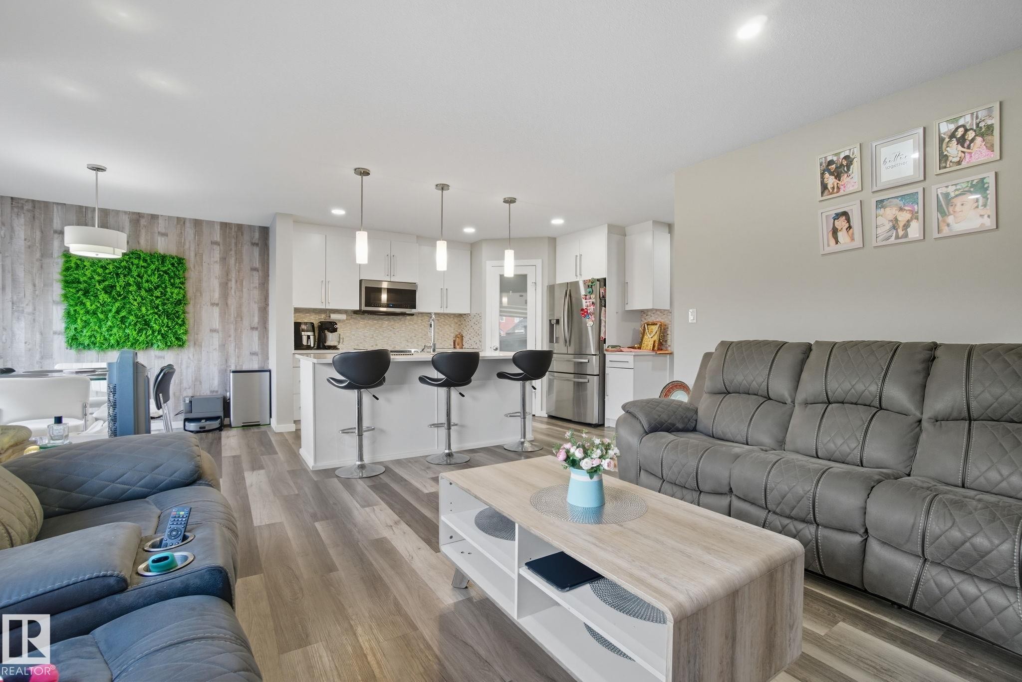 Open-concept living space featuring wood-finish flooring, recessed lighting, white kitchen cabinetry, a kitchen island with pendant lighting, and stainless steel appliances - 2039 Wonnacott Way, Edmonton, AB