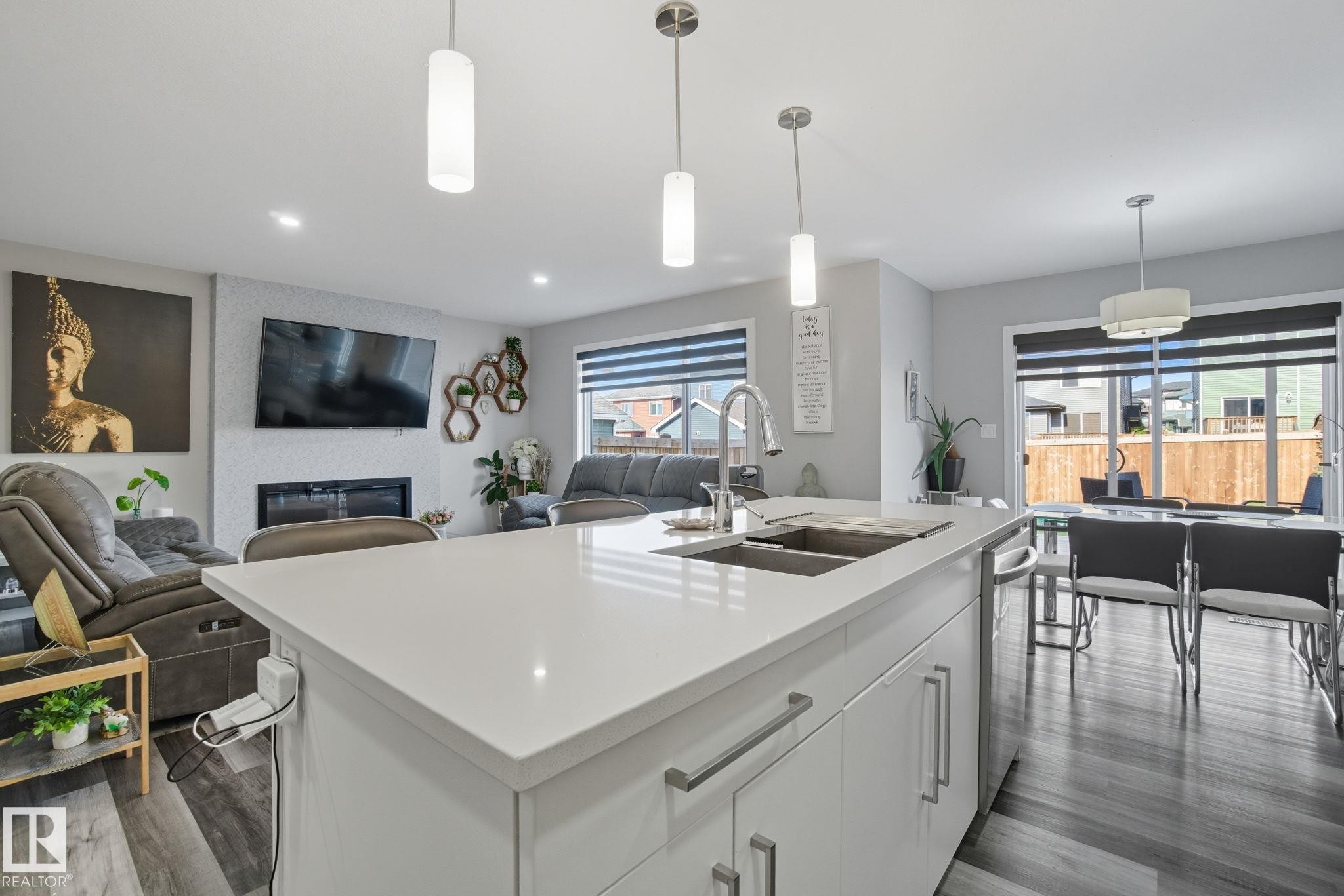 Kitchen island with integrated double sink, modern faucet, and three pendant lights - 2039 Wonnacott Way, Edmonton, AB