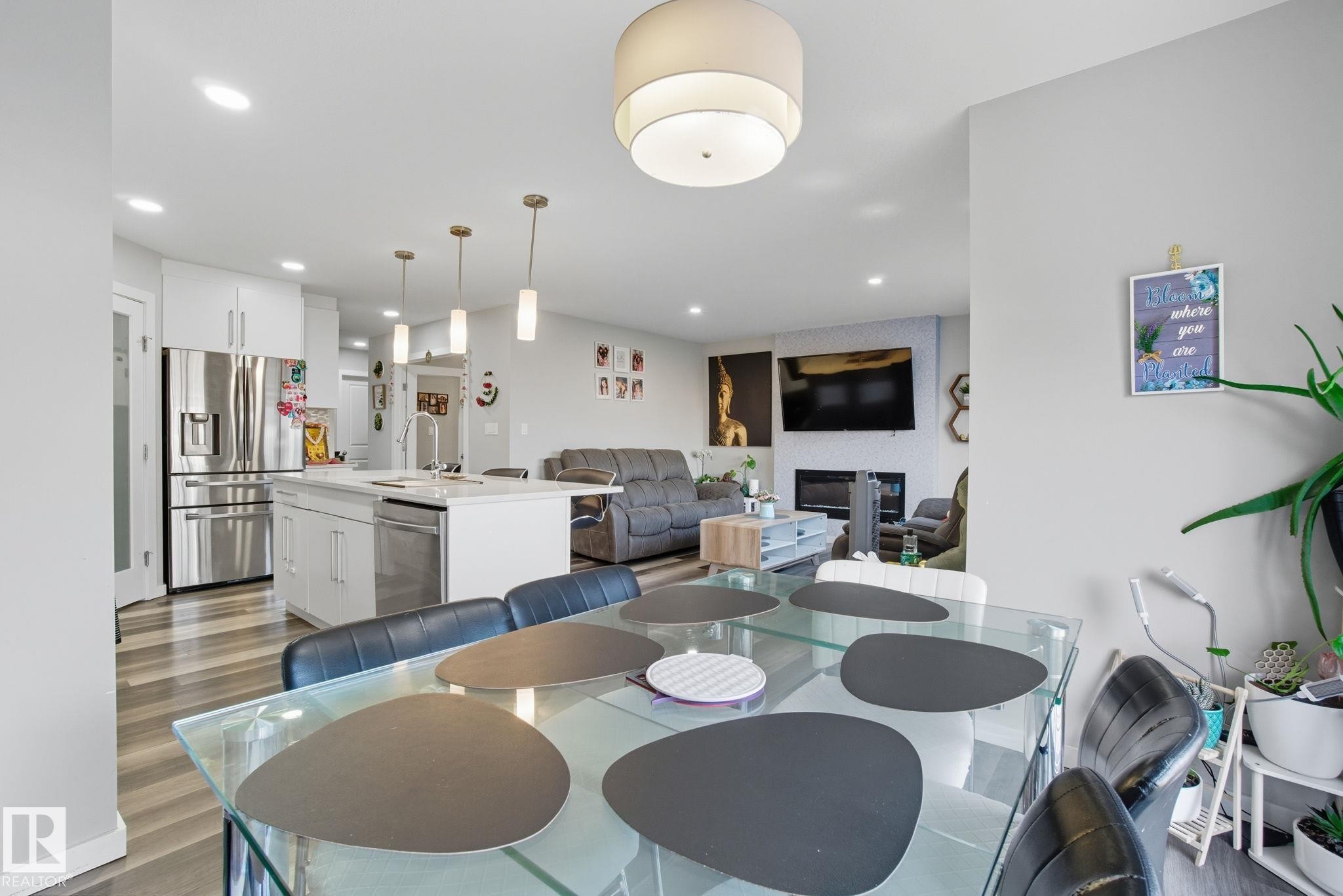 Open-concept interior featuring wood-finish flooring, a contemporary kitchen with white cabinetry and stainless steel appliances, a kitchen island with pendant lighting, recessed lighting, and a living area with a built-in fireplace - 2039 Wonnacott Way, Edmonton, AB