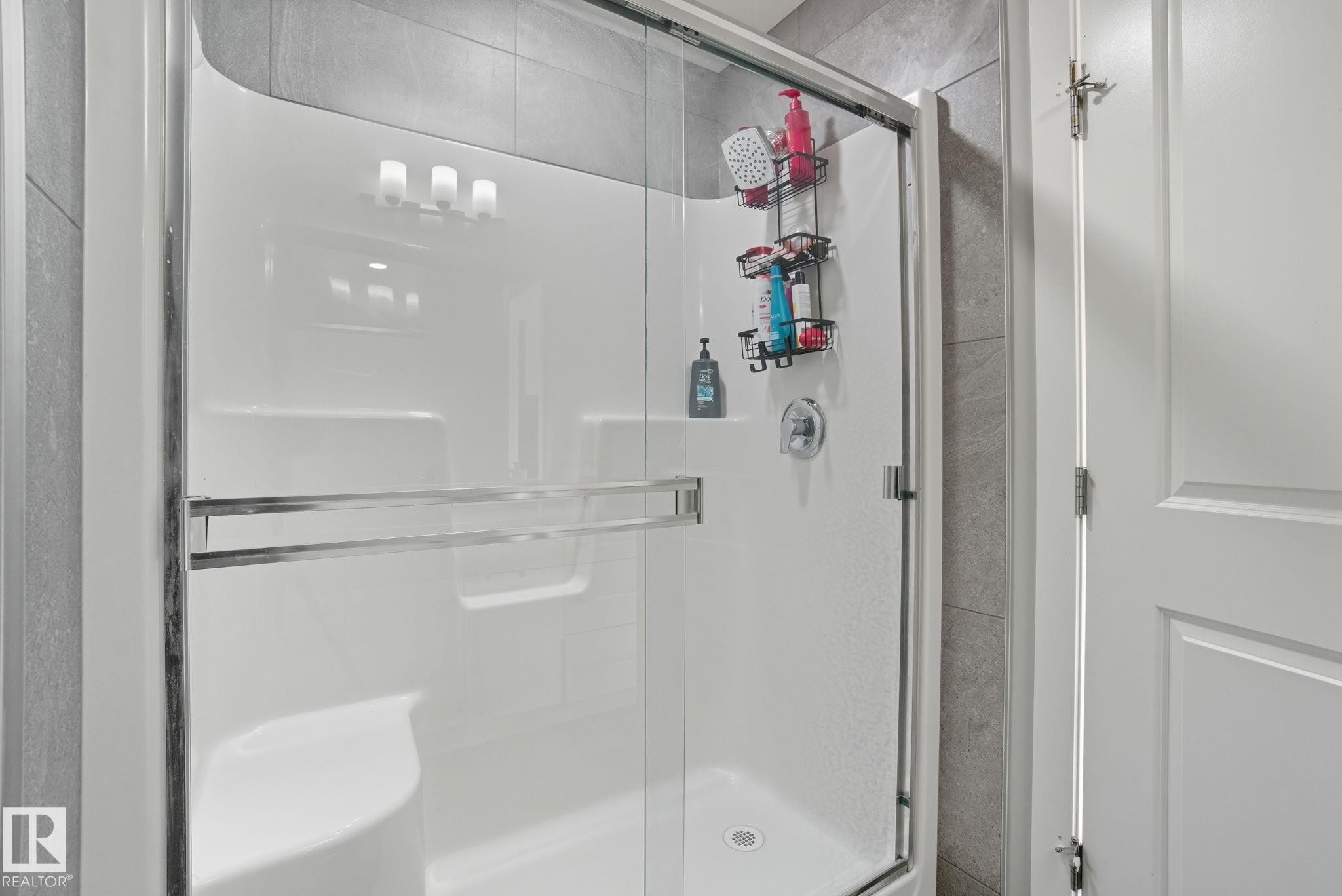 Modern shower enclosure with clear glass doors, chrome hardware, and a built-in bench - 2039 Wonnacott Way, Edmonton, AB