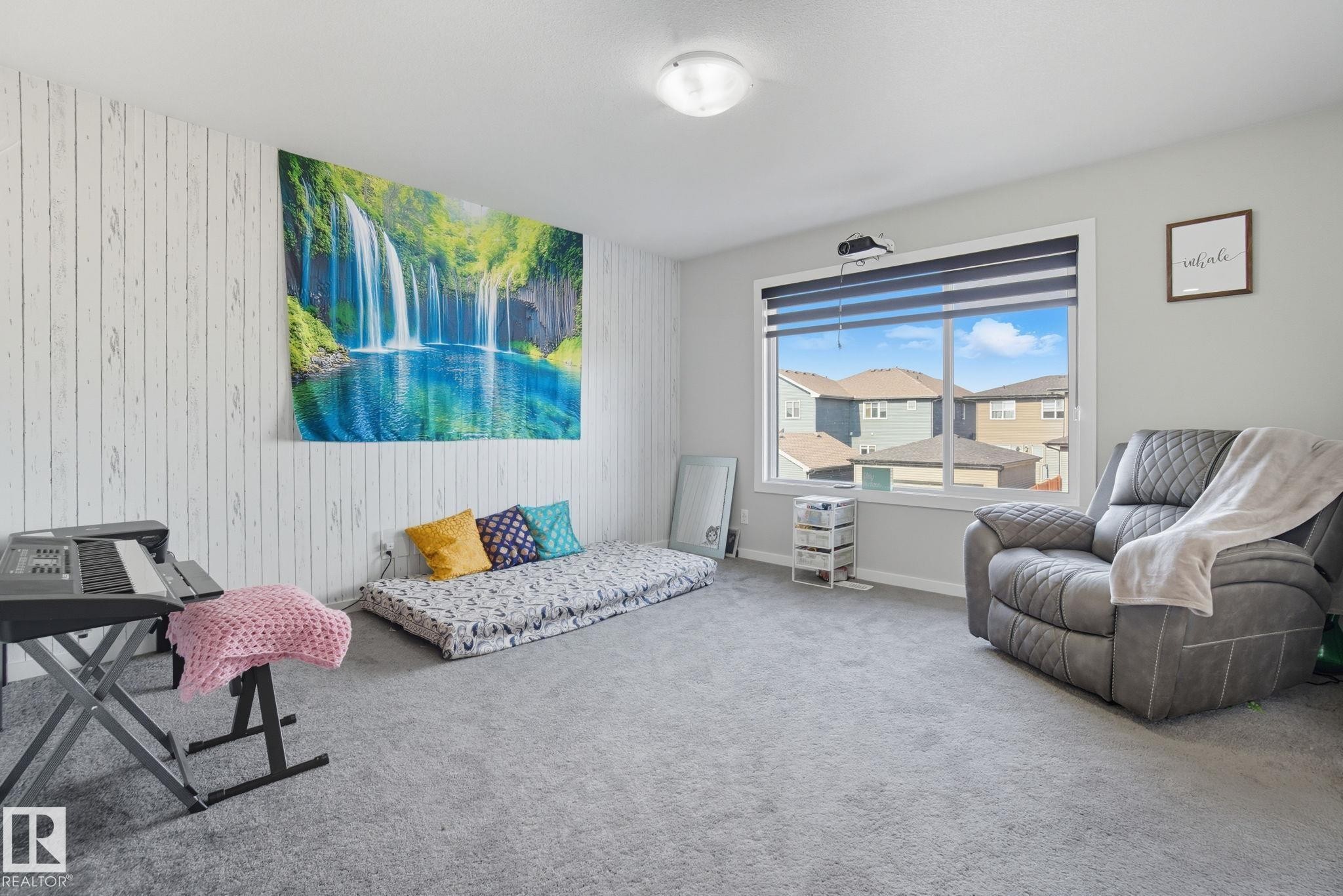 Carpeted interior space featuring a large window, a ceiling-mounted light fixture, white walls, and a feature wall with a vertical plank-style finish - 2039 Wonnacott Way, Edmonton, AB