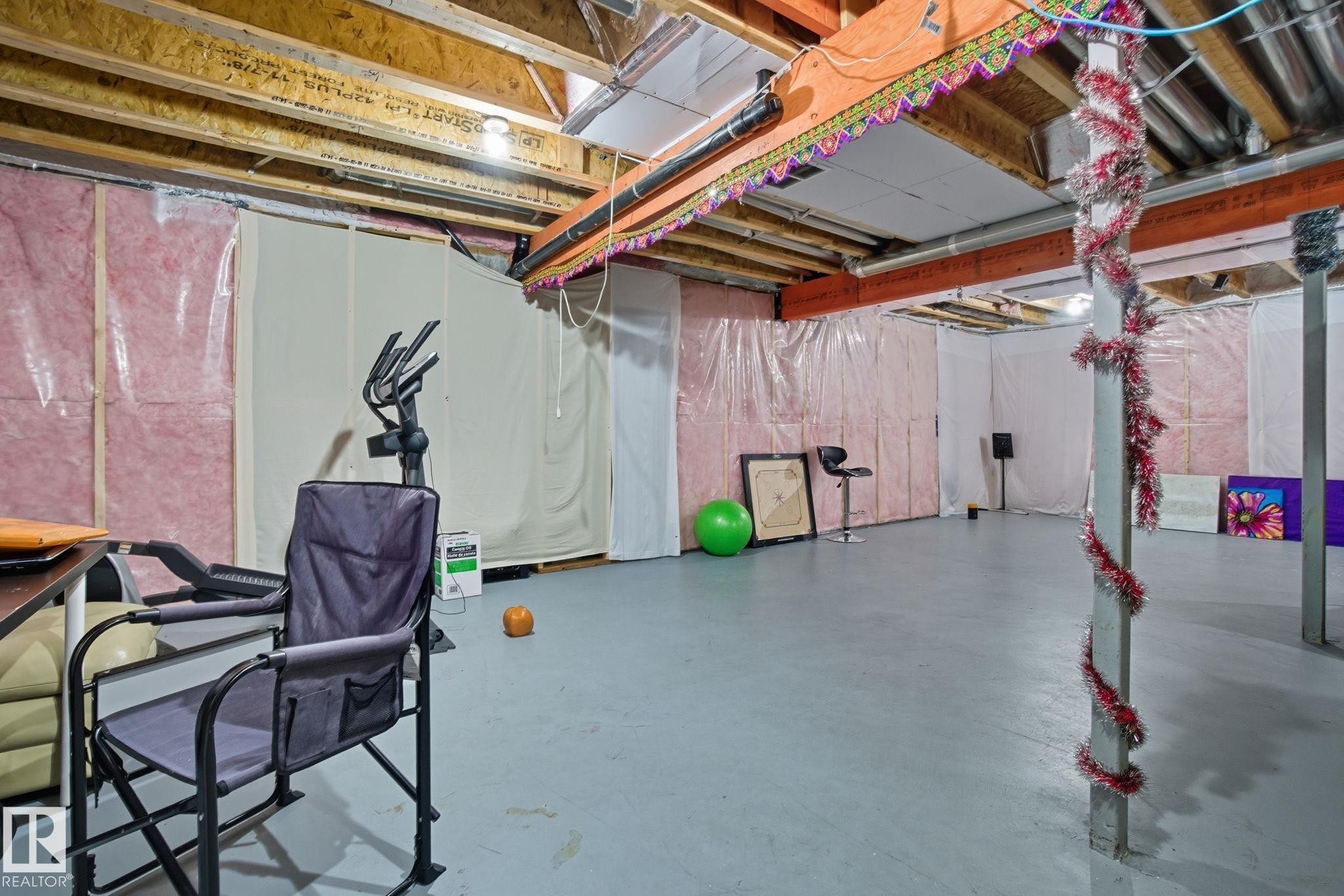 Unfinished basement offering exposed wood beams, pink insulation, and a painted concrete floor - 2039 Wonnacott Way, Edmonton, AB