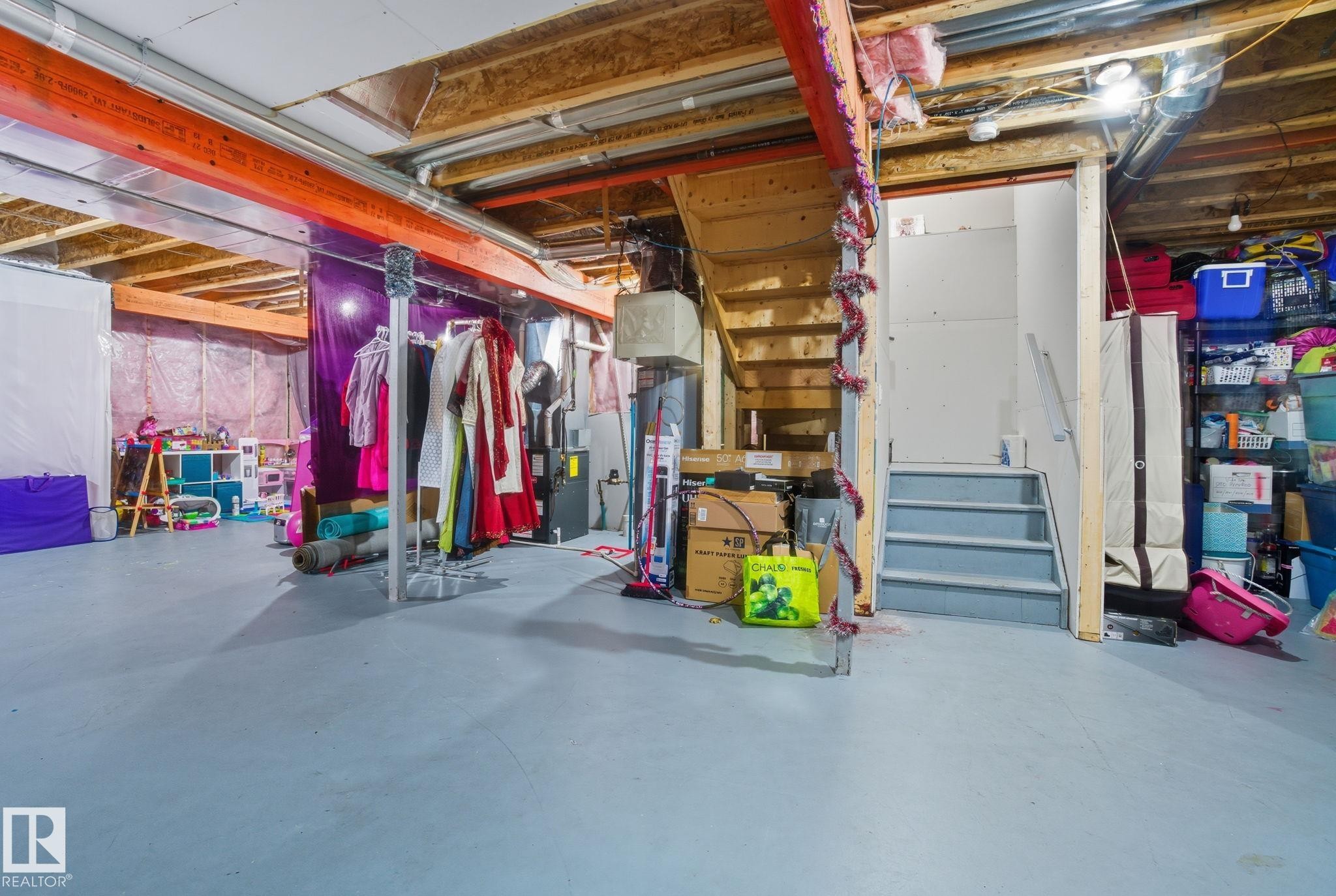 Unfinished lower level with exposed wooden joists and structural beams, featuring concrete flooring, a wooden staircase, and additional storage space - 2039 Wonnacott Way, Edmonton, AB