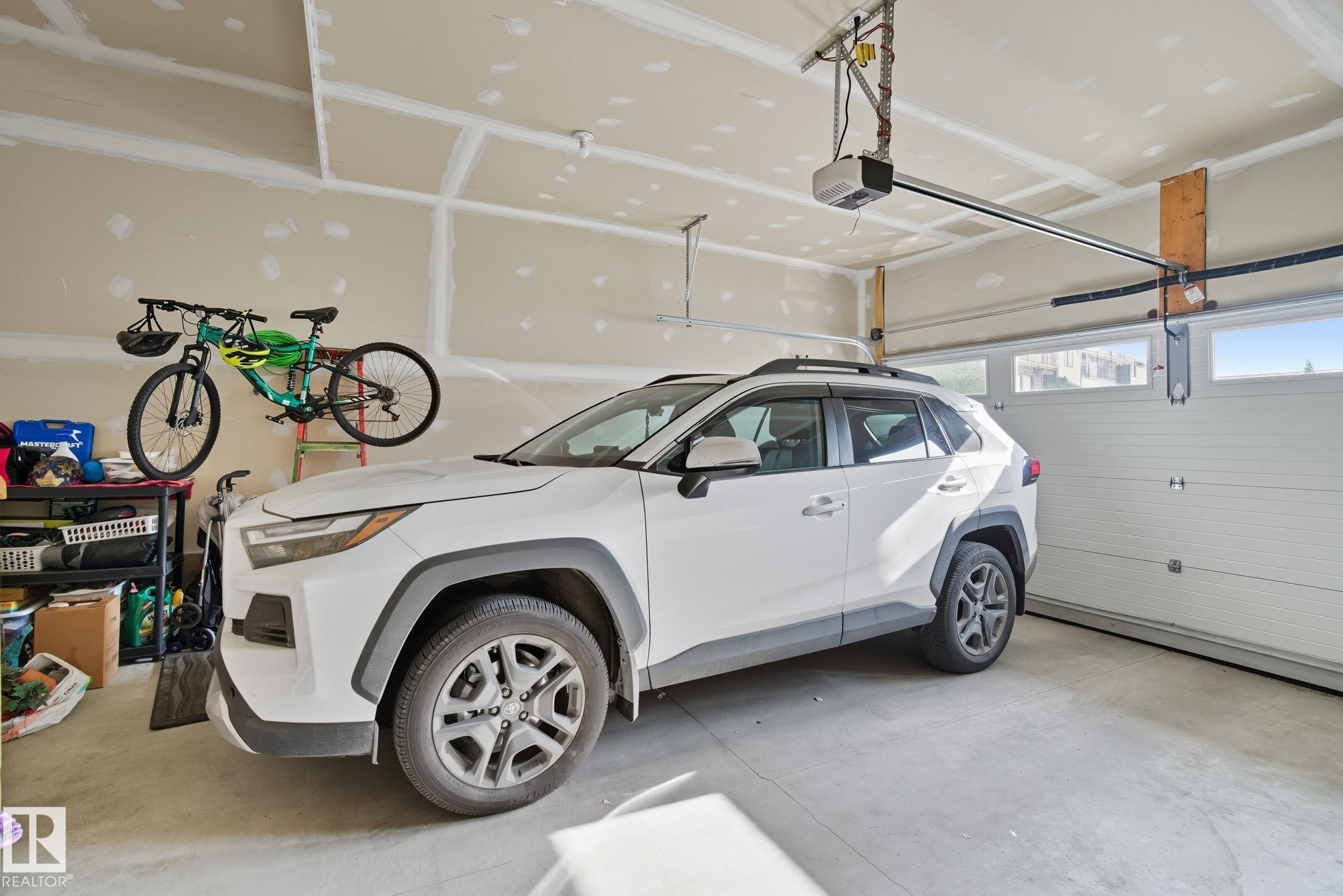 Attached garage featuring a concrete floor, automatic garage door opener, and a white paneled garage door with upper-level windows - 2039 Wonnacott Way, Edmonton, AB
