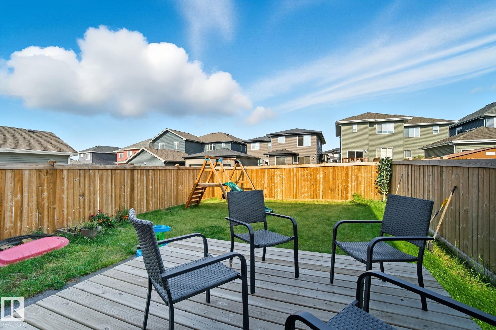 Expansive backyard featuring a natural wood fence, a spacious deck, and a green lawn - 2039 Wonnacott Way, Edmonton, AB