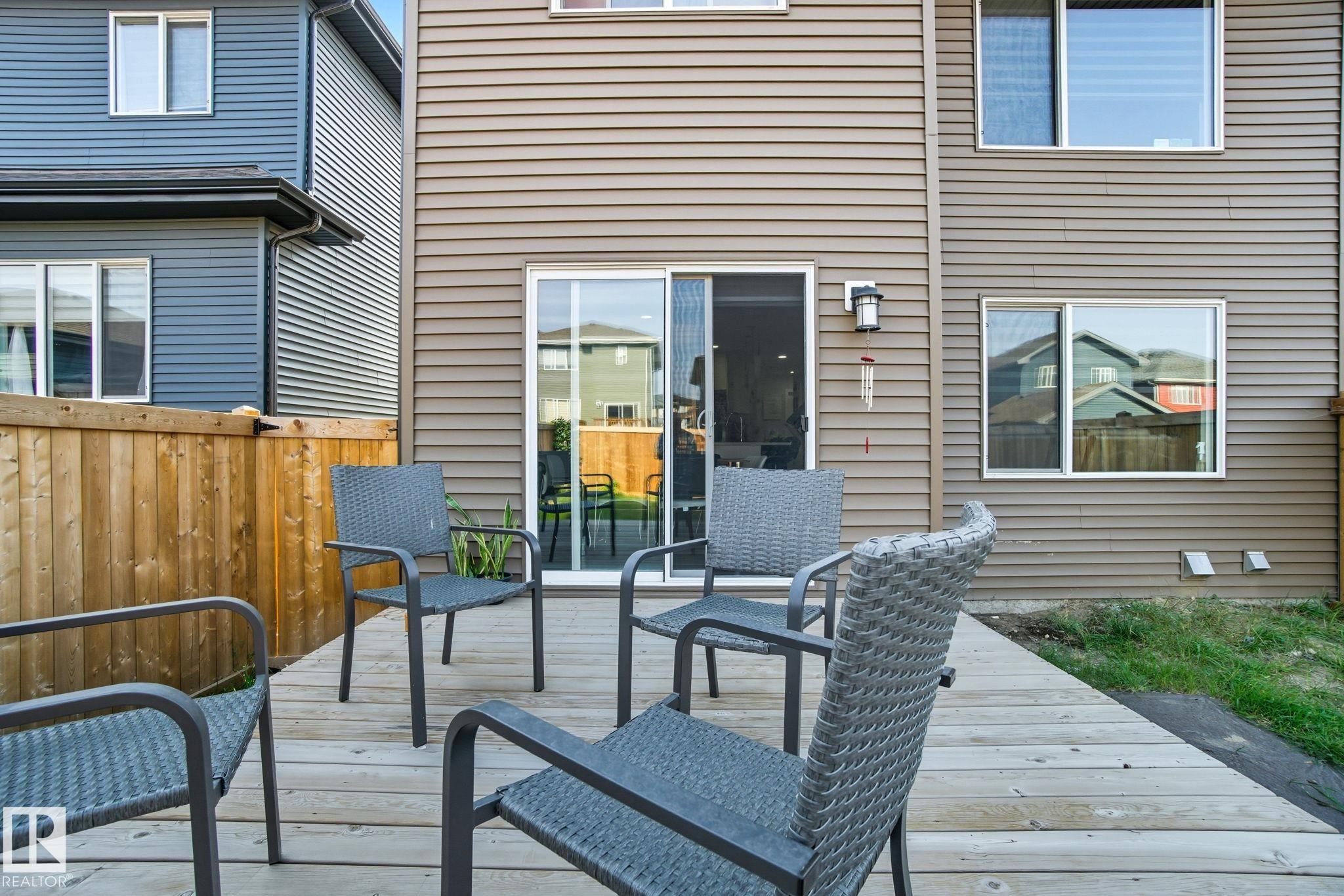 Private outdoor deck with a sliding glass door entry to the home, featuring horizontal siding, a wooden fence, and multiple windows - 2039 Wonnacott Way, Edmonton, AB