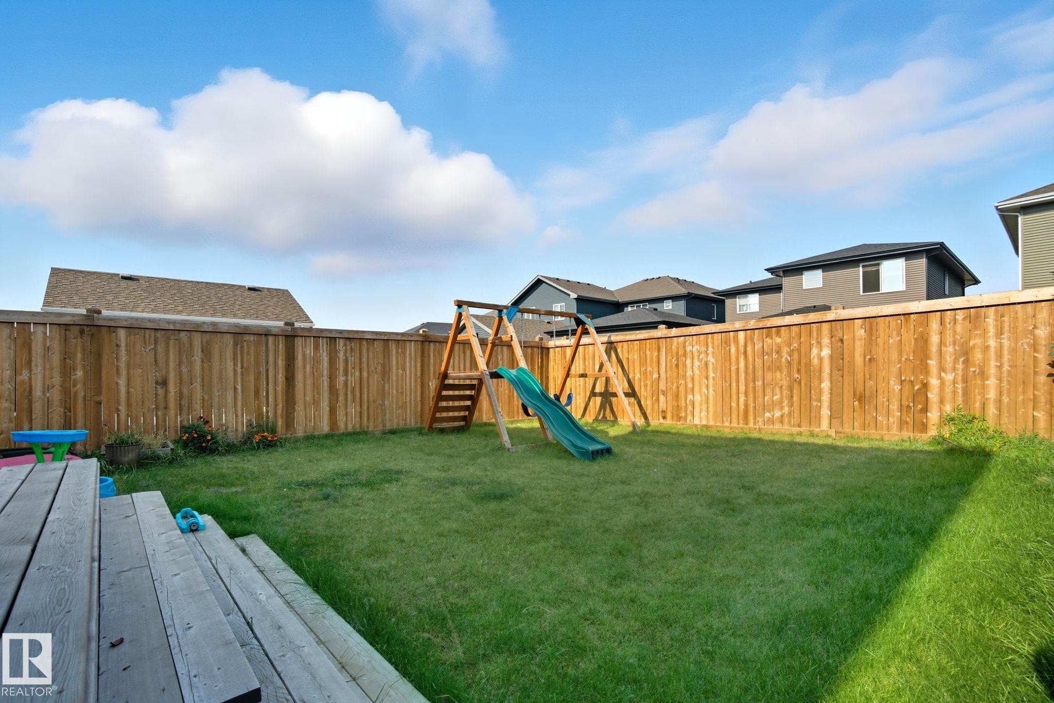 Expansive backyard featuring a green lawn, wood deck, and full-height wood fencing - 2039 Wonnacott Way, Edmonton, AB