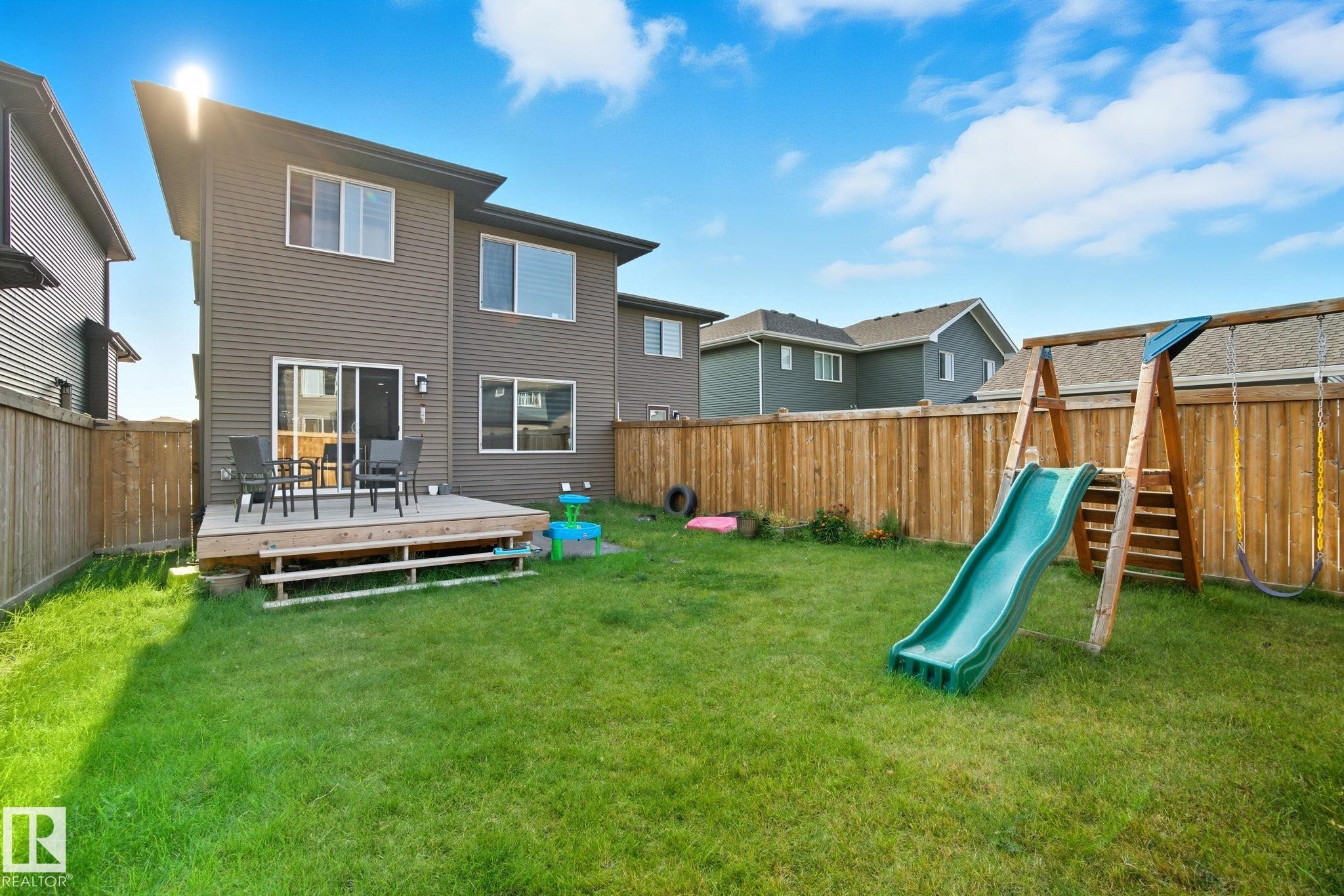 Expansive green lawn with a wooden privacy fence, featuring a raised deck with wooden steps and a sliding glass door - 2039 Wonnacott Way, Edmonton, AB