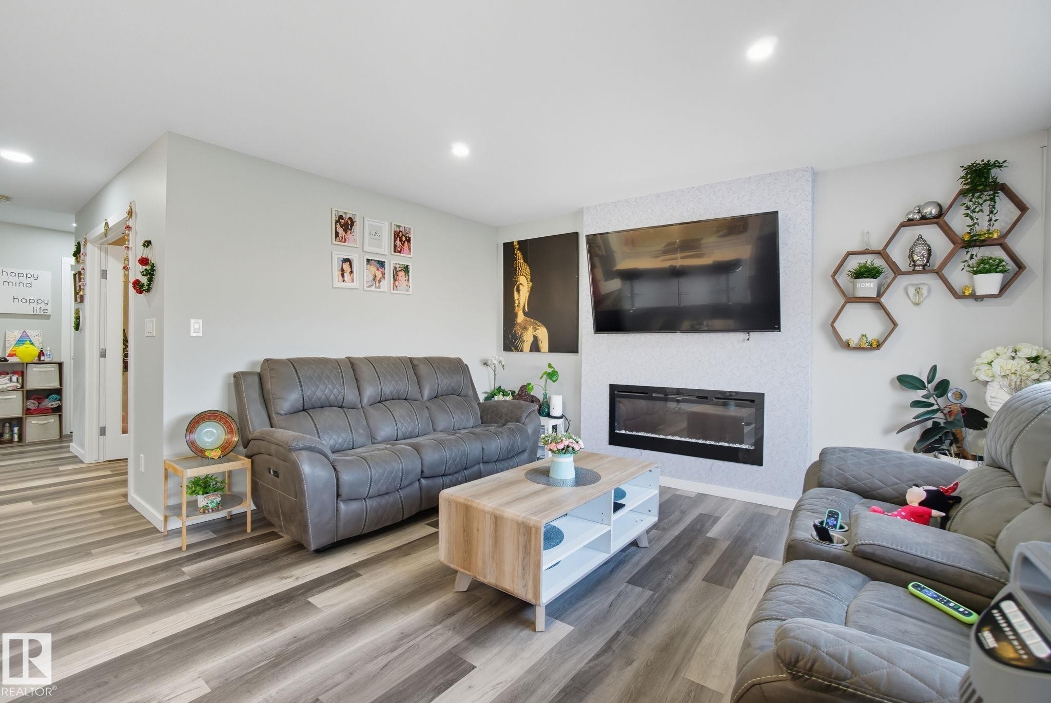 Living area featuring wood-finish flooring, recessed lighting, and a wall-mounted electric fireplace with a textured accent wall - 2039 Wonnacott Way, Edmonton, AB
