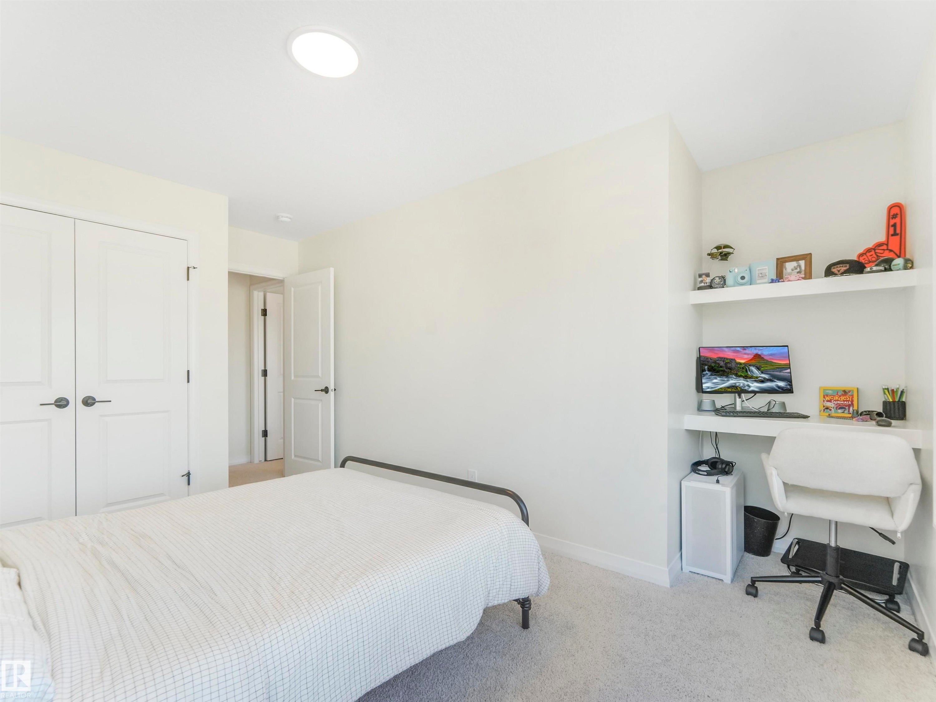 This room features light-colored walls and carpet, a circular ceiling light fixture, and two paneled doors with dark hardware - 19 Nettle Crescent, St. Albert, AB - Indoor Photo Showing Bedroom