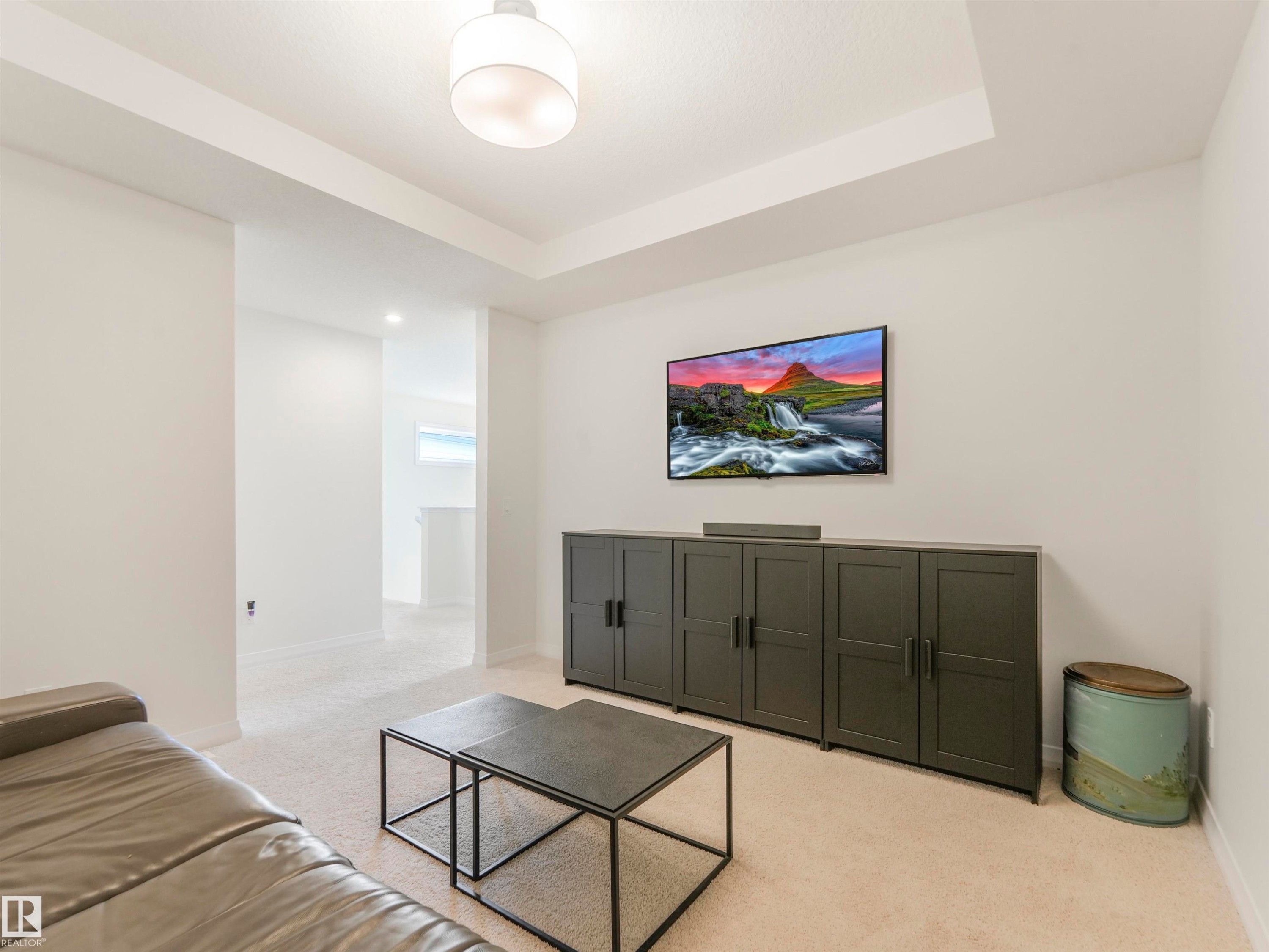 This living space features a tray ceiling, light-colored carpeting, and a recessed wall for media - 19 Nettle Crescent, St. Albert, AB - Indoor