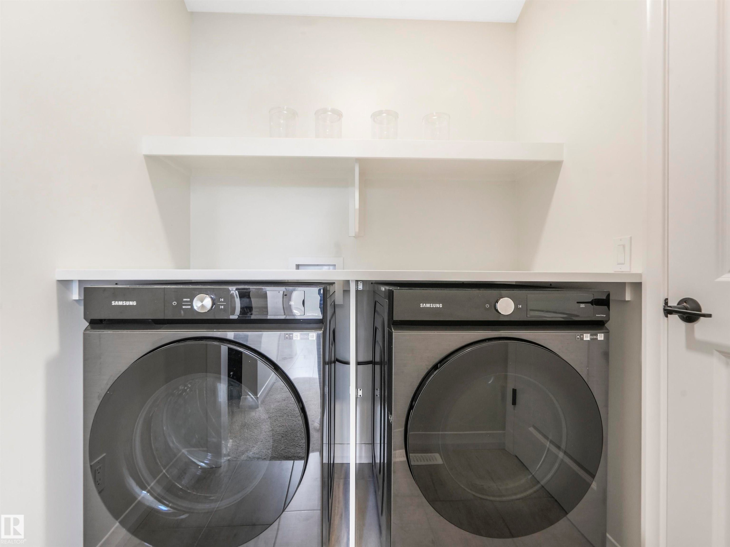 Dedicated laundry area featuring a white floating shelf, countertop space, and black front-loading appliances - 19 Nettle Crescent, St. Albert, AB - Indoor Photo Showing Laundry Room