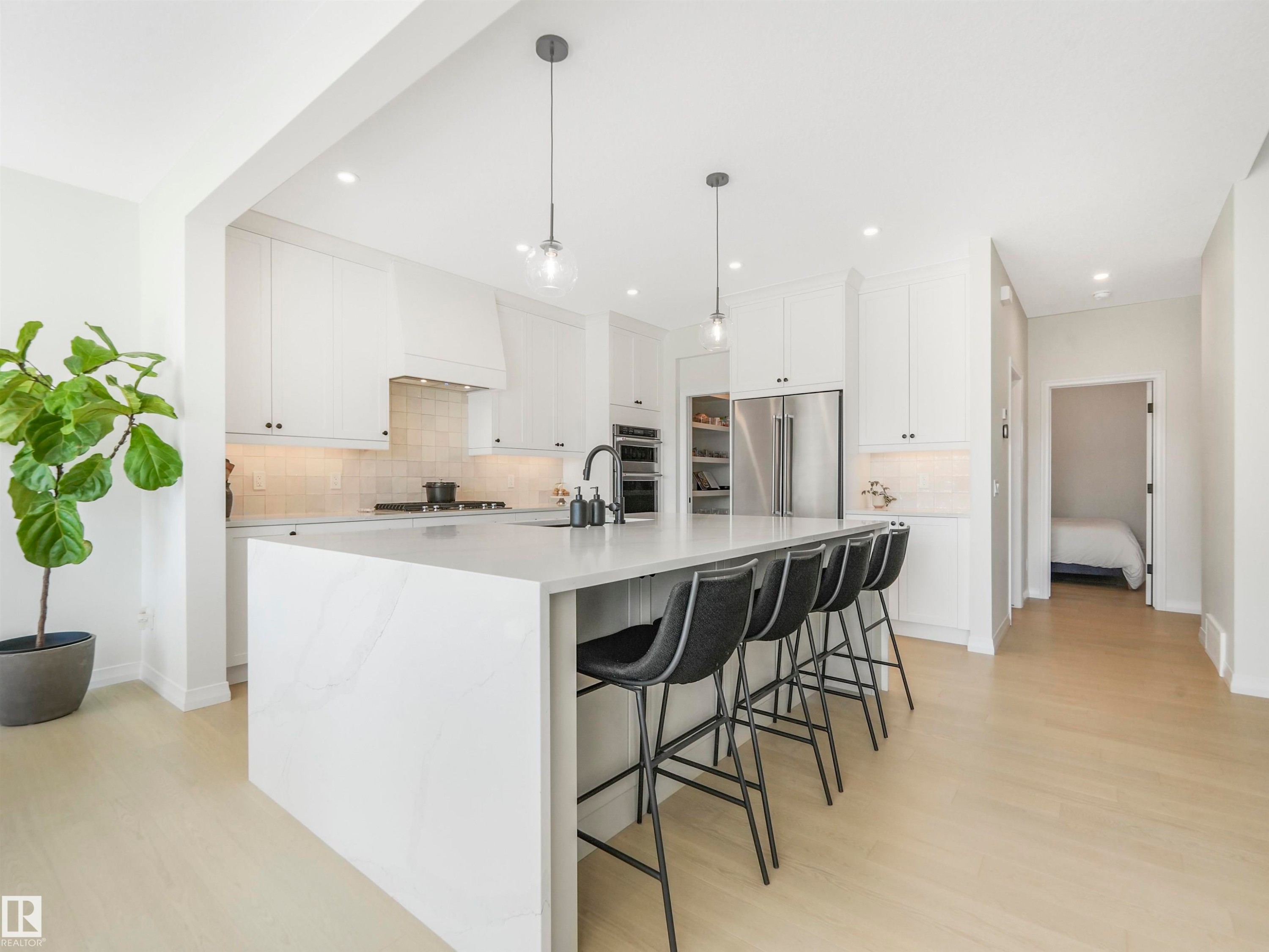This bright kitchen features white cabinetry, stainless steel appliances, a large island with seating, and light-colored flooring - 19 Nettle Crescent, St. Albert, AB - Indoor Photo Showing Kitchen With Upgraded Kitchen