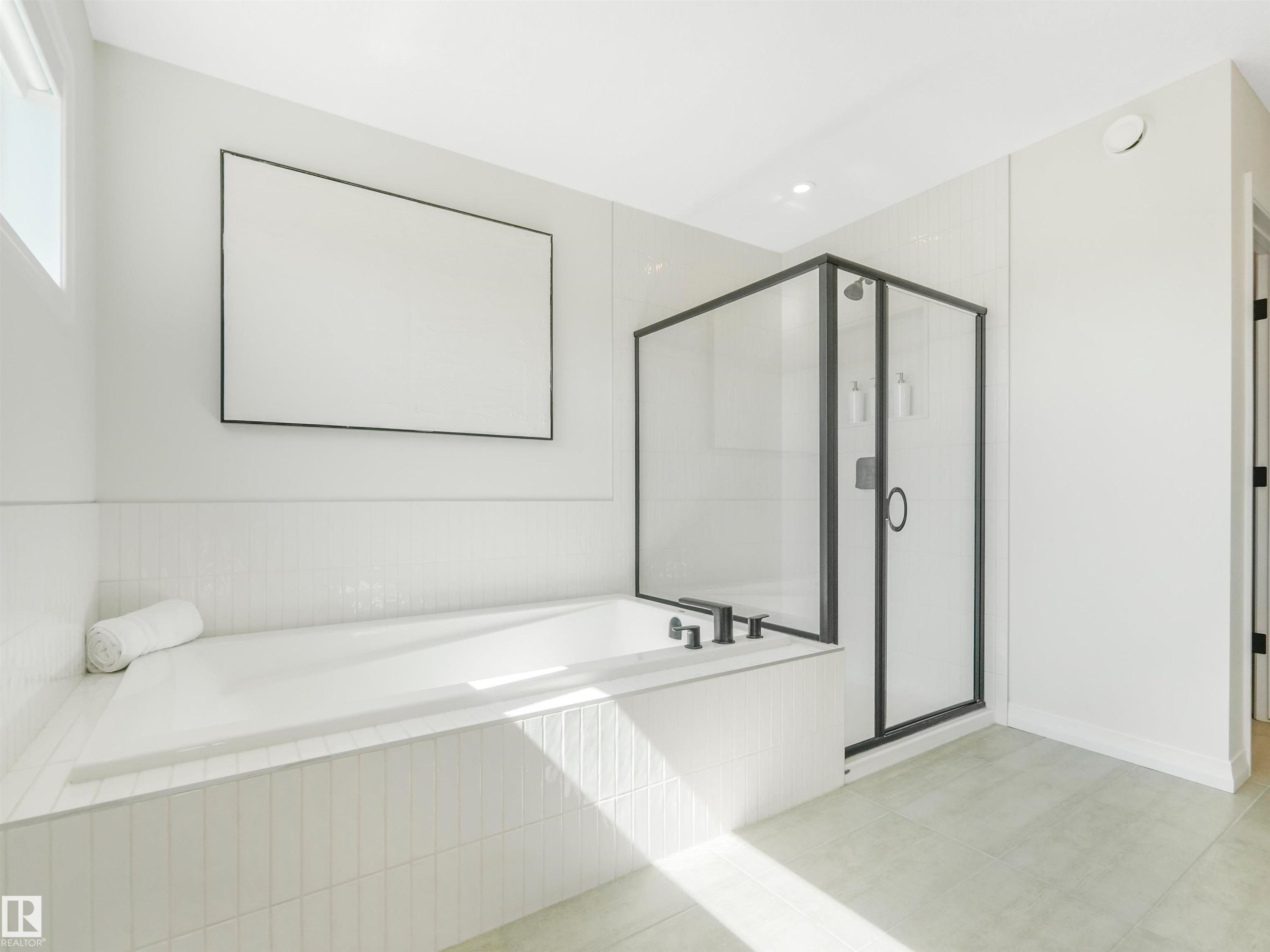 The bathroom features a built-in bathtub with a tiled surround, a separate glass-enclosed shower with black trim, and light-colored flooring - 19 Nettle Crescent, St. Albert, AB - Indoor Photo Showing Bathroom
