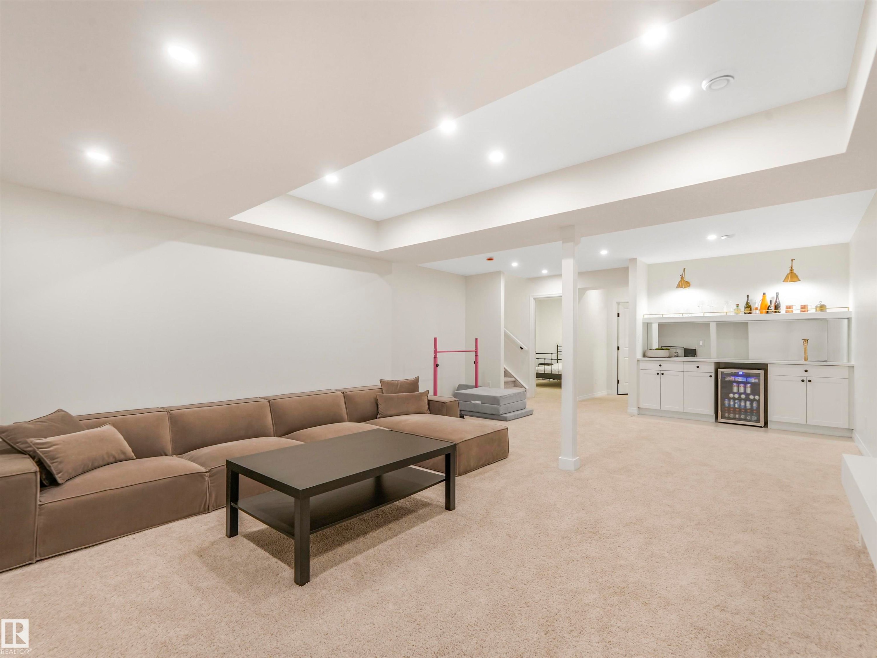 This expansive recreation room features recessed lighting, carpeted flooring, and a built-in wet bar with white cabinetry and a beverage cooler - 19 Nettle Crescent, St. Albert, AB - Indoor