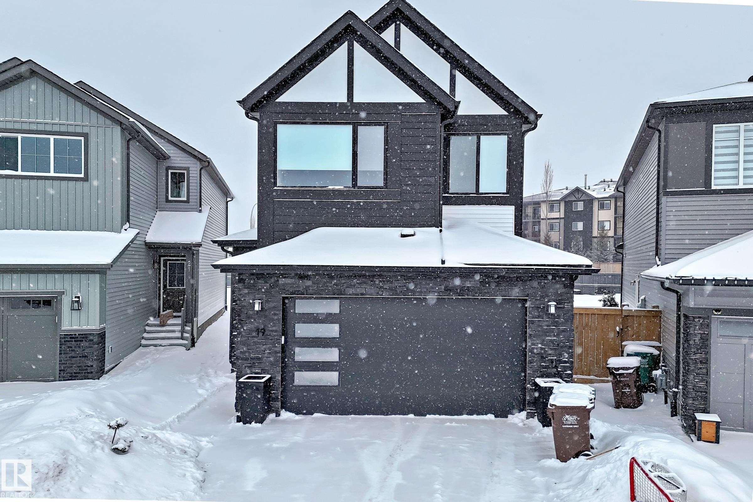The property features a contemporary exterior with dark siding and white trim, an integrated garage with a modern door, and a paved driveway - 19 Nettle Crescent, St. Albert, AB - Outdoor