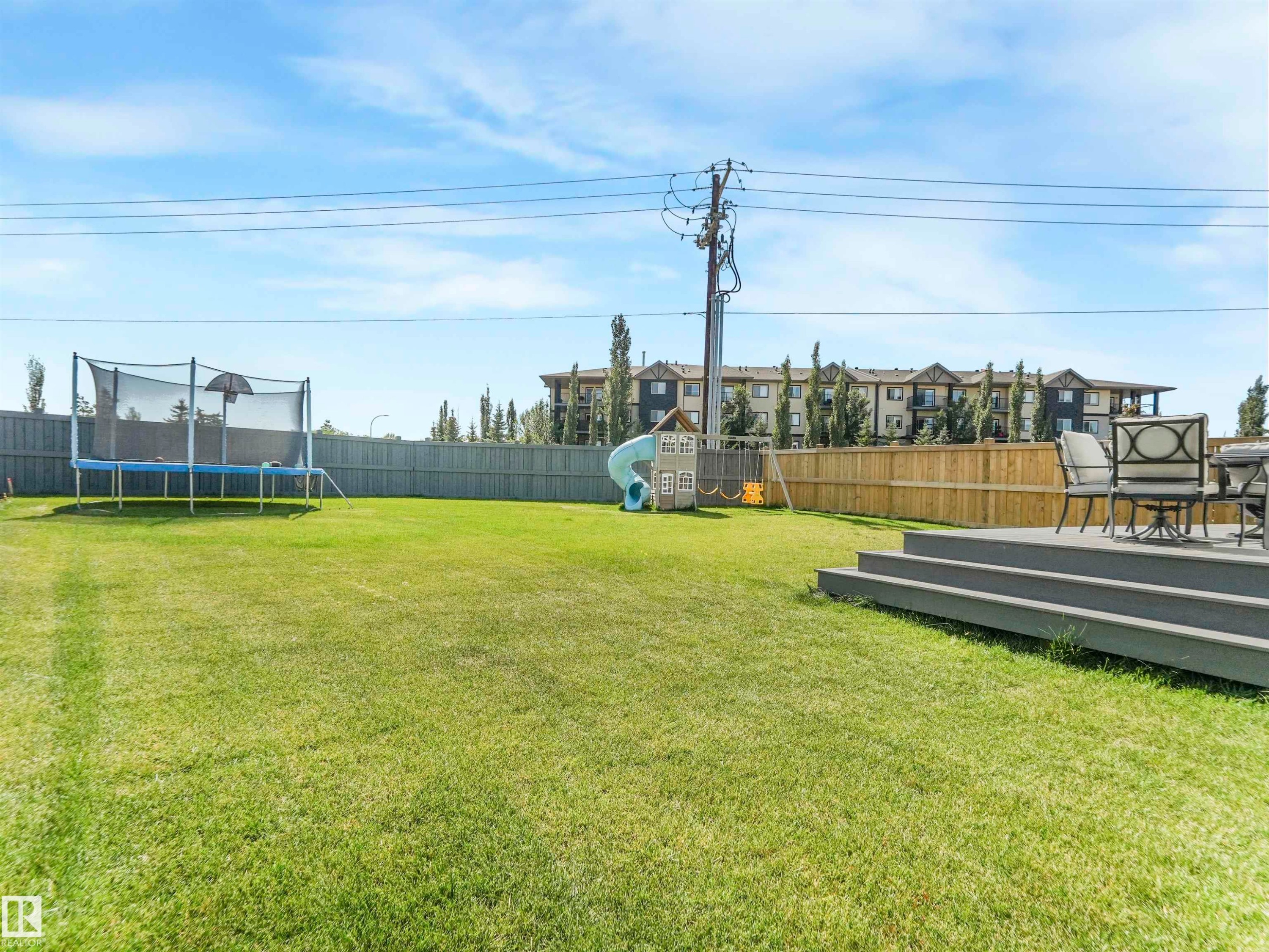 The property features an expansive lawn, a privacy fence, and a multi-tiered deck with ample space for outdoor seating - 19 Nettle Crescent, St. Albert, AB - Outdoor