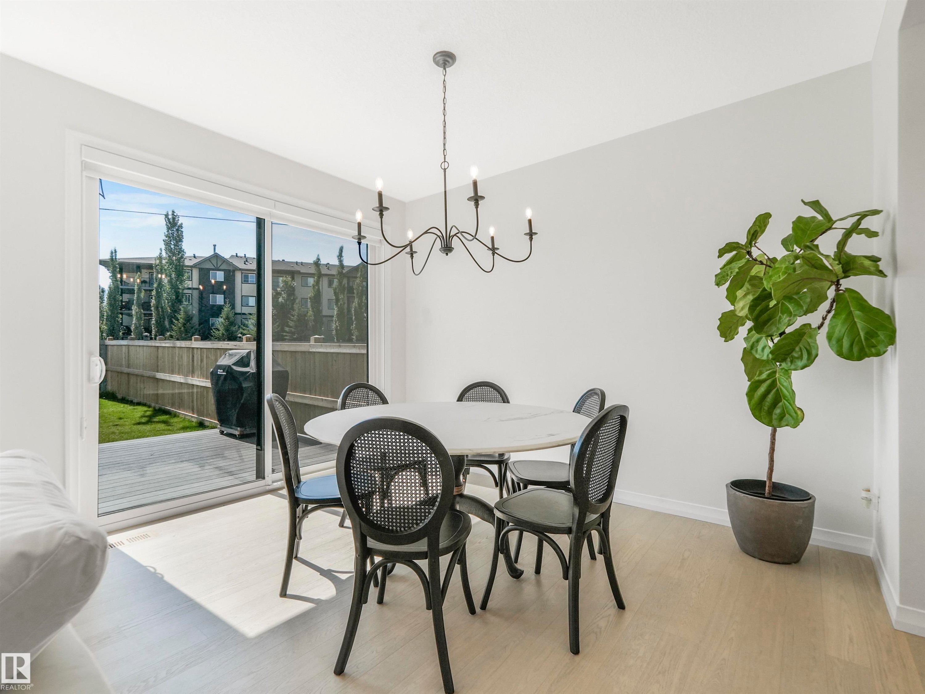 The dining area features light-colored flooring, a modern chandelier, and access to an outdoor deck and yard through sliding glass doors - 19 Nettle Crescent, St. Albert, AB - Indoor Photo Showing Dining Room