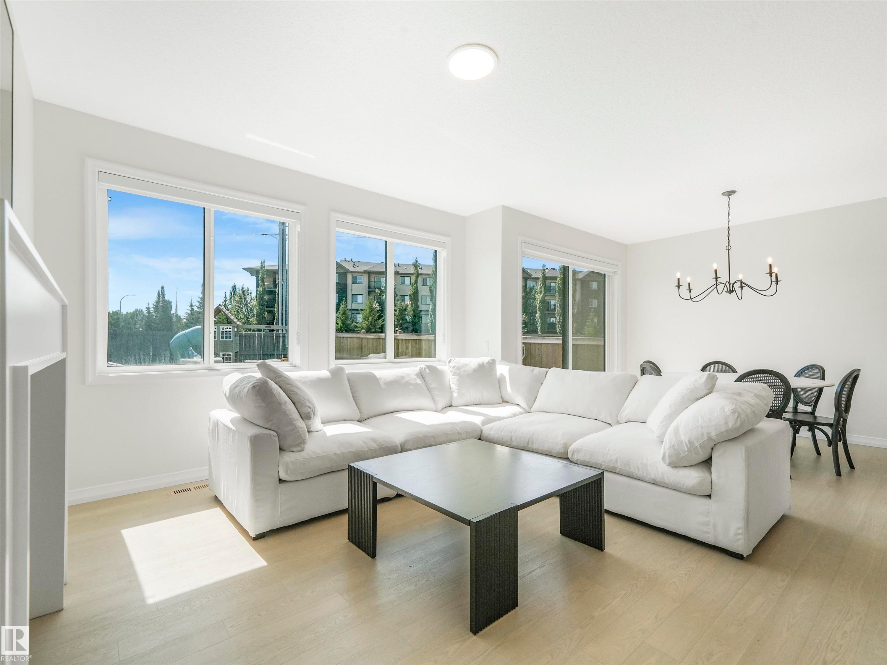 Bright and inviting living space featuring light-toned flooring, large windows, and a dining area with a chandelier - 19 Nettle Crescent, St. Albert, AB - Indoor Photo Showing Living Room