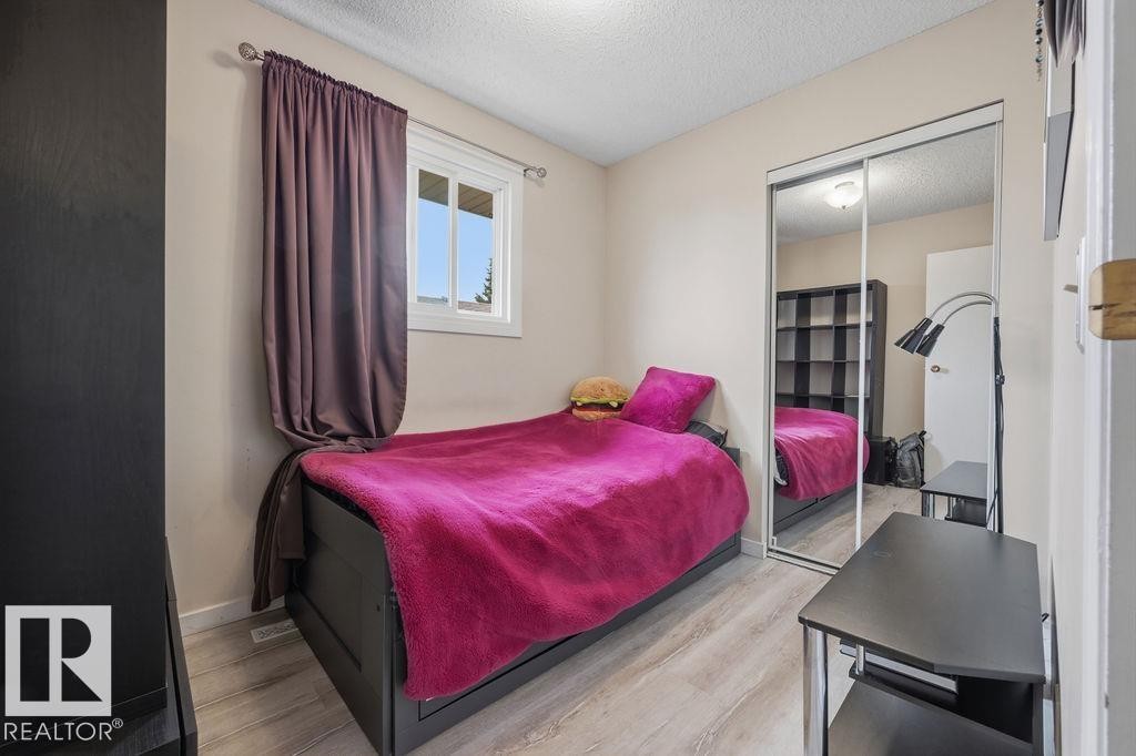 Bedroom featuring a window with a white frame, wood-finish flooring, and a mirrored sliding closet door - 7422 188 Street, Edmonton, AB