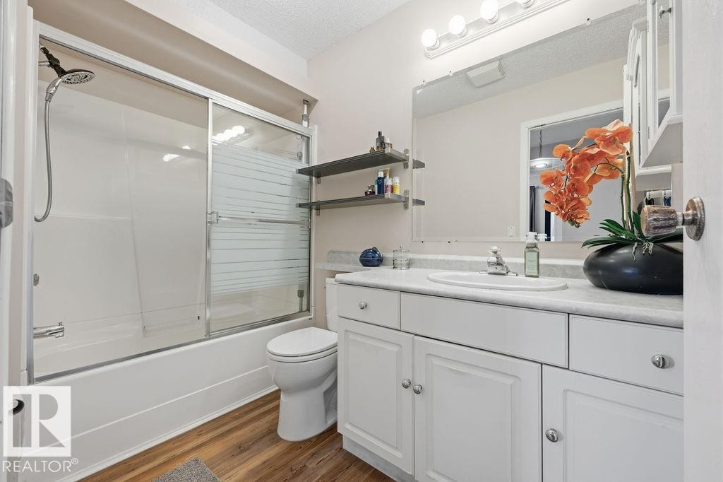 Bathroom featuring a white vanity with integrated sink, a large wall-mounted mirror, and a combination bathtub and shower with sliding glass doors - 7422 188 Street, Edmonton, AB