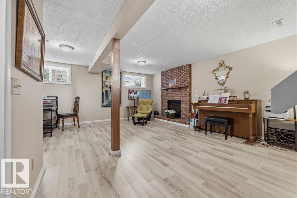Spacious room featuring light wood-finish flooring, a brick fireplace with a wood mantel, and overhead recessed lighting - 7422 188 Street, Edmonton, AB