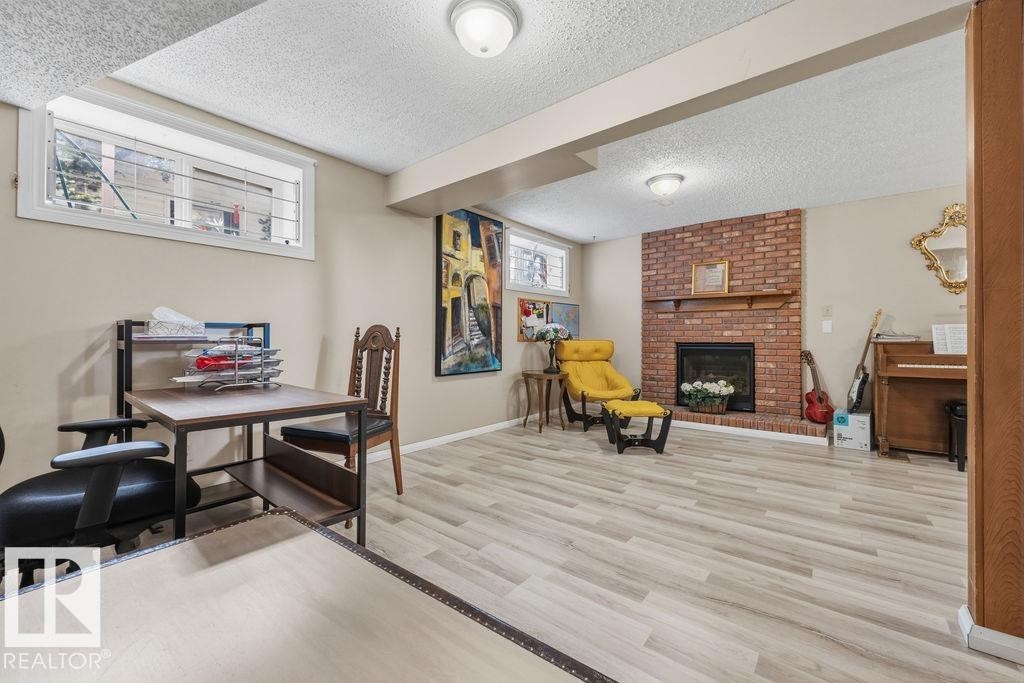 Finished space featuring light wood-finish flooring, a brick fireplace with a wood mantle, recessed windows with security bars, and ceiling-mounted lighting - 7422 188 Street, Edmonton, AB