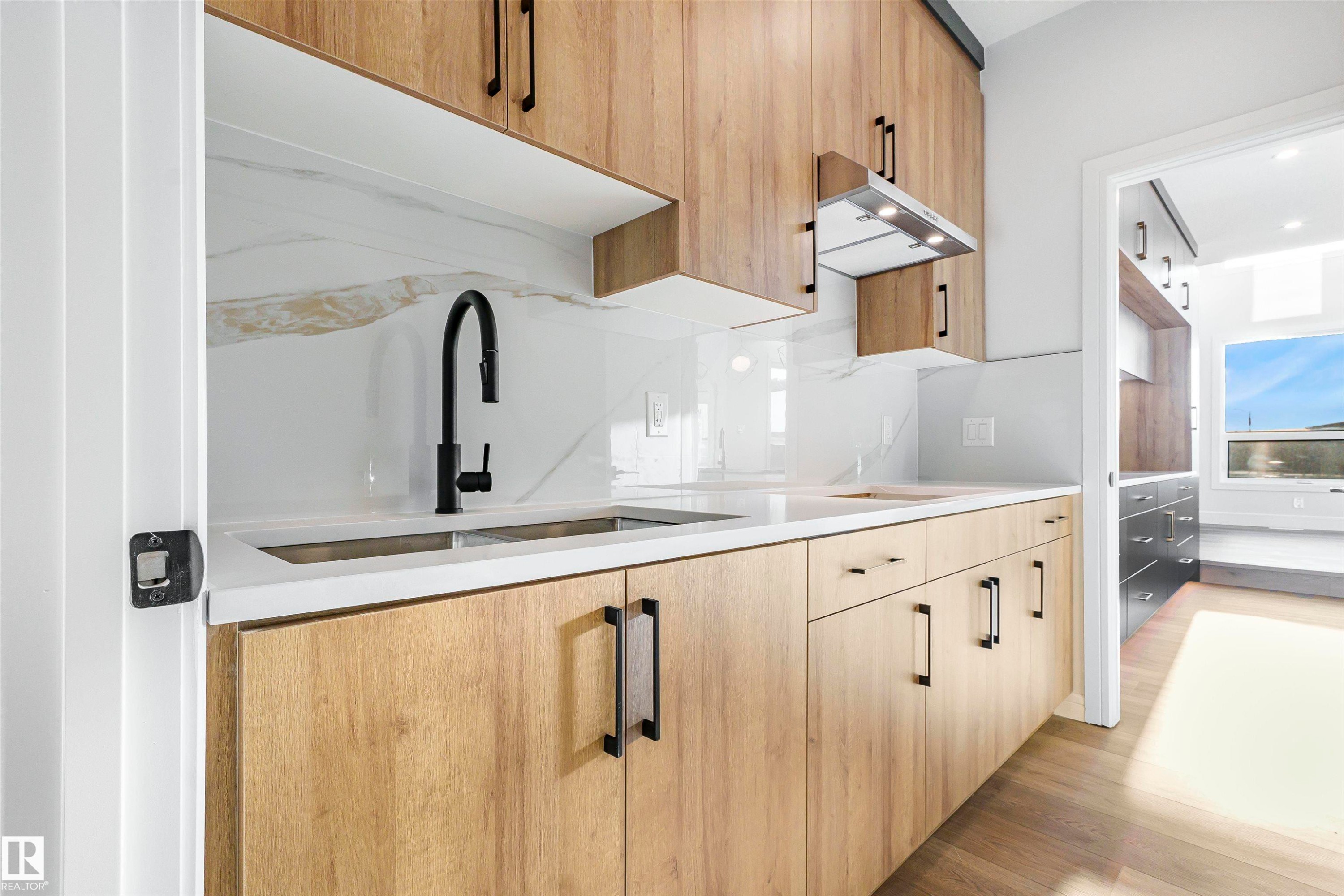 Modern kitchen featuring wood-finish cabinetry with matte black hardware, white countertops, and a white marble-patterned backsplash - 372 Creekside Green, Leduc, AB - Indoor Photo Showing Kitchen