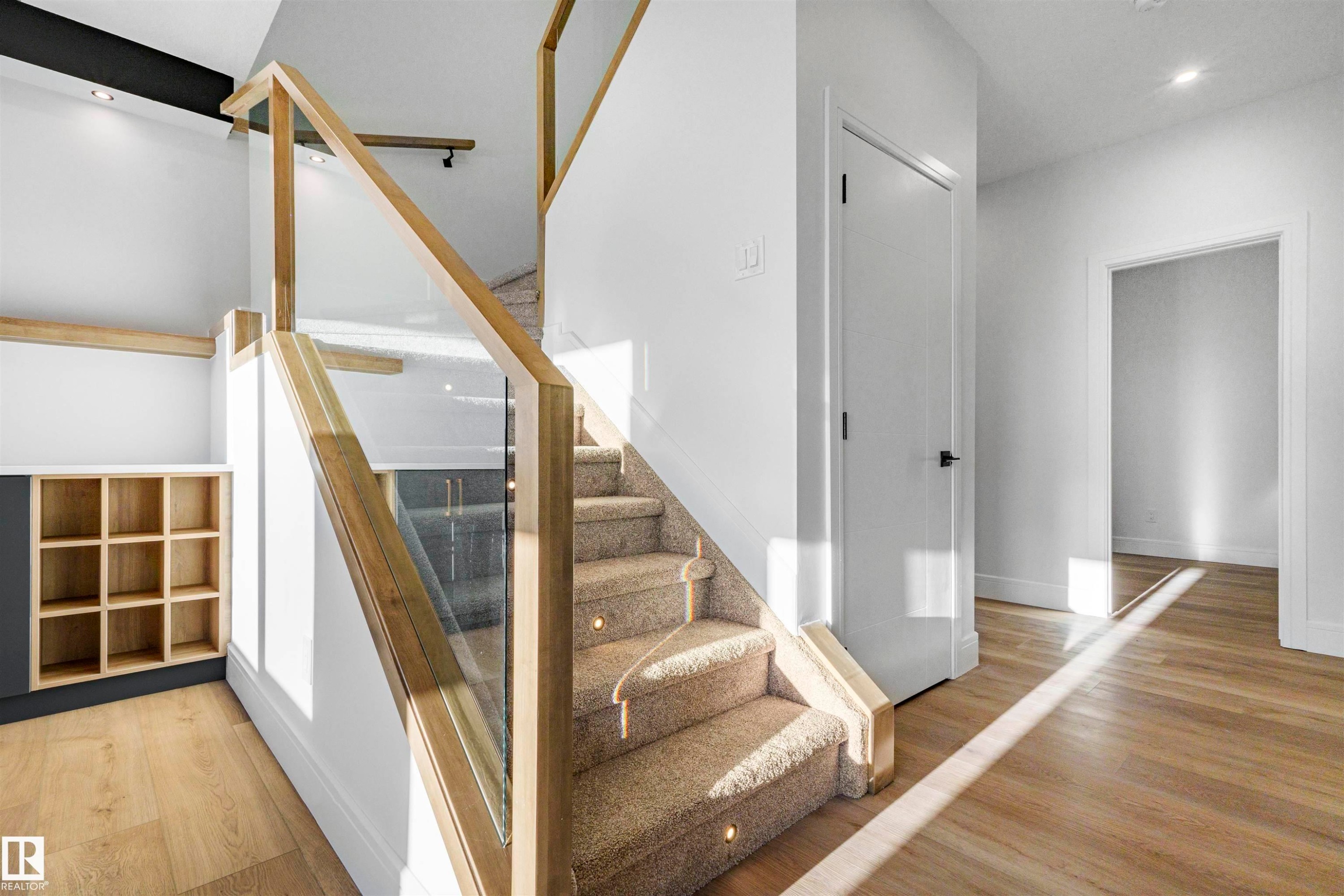 Carpeted staircase with integrated step lighting and glass railing system, featuring wood-finish handrails - 372 Creekside Green, Leduc, AB - Indoor Photo Showing Other Room