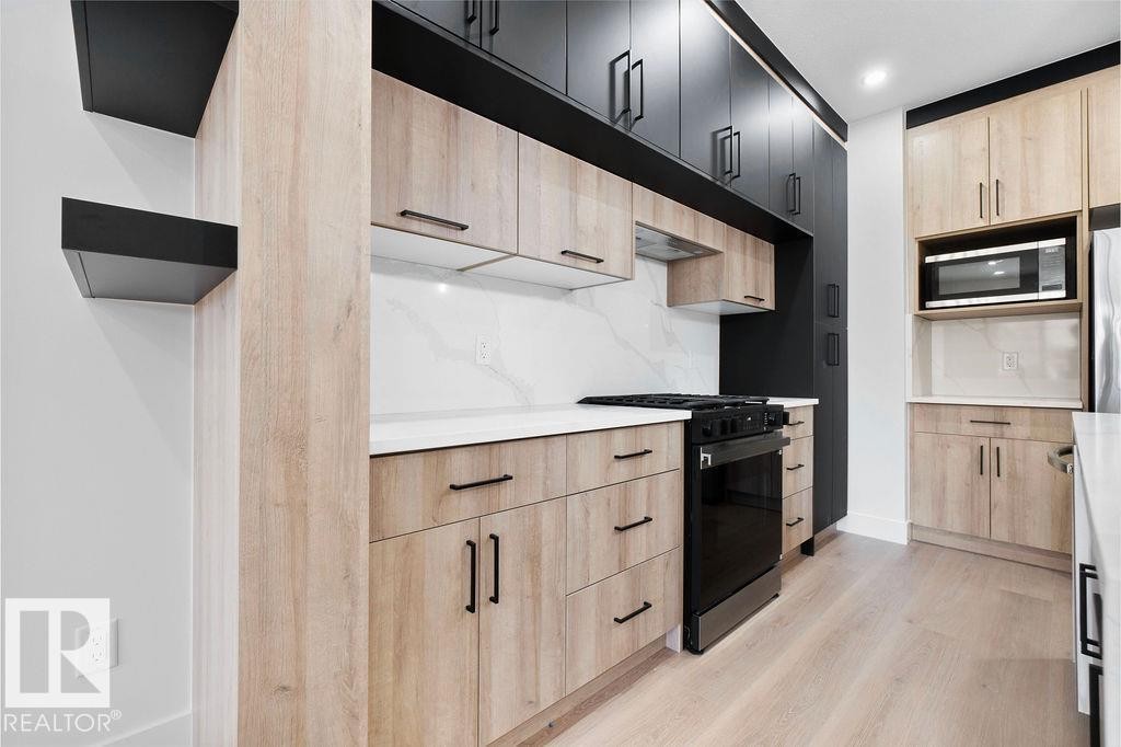 The kitchen features light wood cabinetry with dark hardware, white countertops, and a full-height white backsplash - 12307 91 St Nw, Edmonton, AB - Indoor Photo Showing Kitchen With Upgraded Kitchen