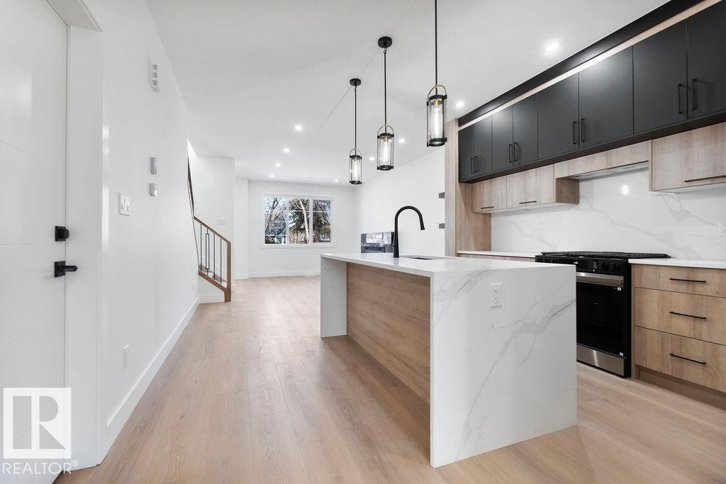 The kitchen features a large island with a waterfall countertop, a matte black faucet, and pendant lighting - 12307 91 St Nw, Edmonton, AB - Indoor Photo Showing Kitchen With Upgraded Kitchen