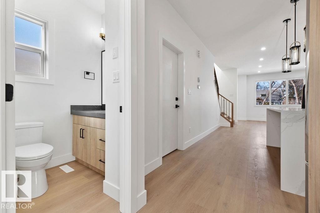Bright interior with light wood flooring and white walls, featuring a bathroom with a window, a vanity with a dark countertop, and a toilet - 12307 91 St Nw, Edmonton, AB - Indoor