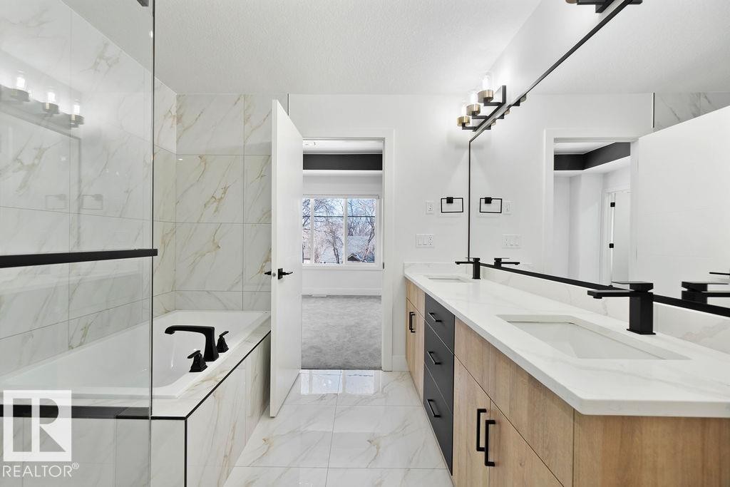 A contemporary bathroom featuring a bathtub with a tiled surround, a glass shower enclosure, and a double vanity with white countertops and matte black fixtures - 12307 91 St Nw, Edmonton, AB - Indoor Photo Showing Bathroom