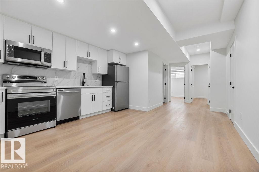 The property features a modern kitchen equipped with stainless steel appliances, white cabinetry, and a marble-patterned backsplash - 12307 91 St Nw, Edmonton, AB - Indoor Photo Showing Kitchen With Stainless Steel Kitchen
