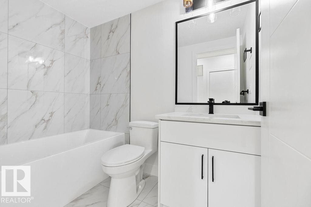 Bathroom featuring a bathtub with tiled walls, a toilet, a vanity with storage, and a mirror - 12307 91 St Nw, Edmonton, AB - Indoor Photo Showing Bathroom