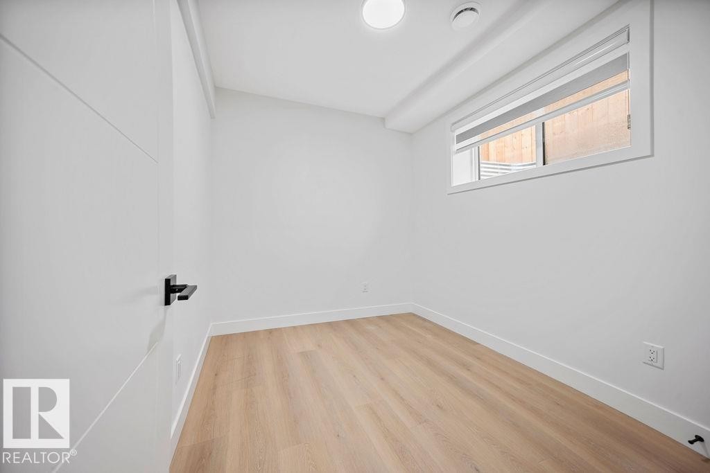 This bright interior room features light-colored flooring, a window, and a white door with a black handle - 12307 91 St Nw, Edmonton, AB - Indoor Photo Showing Other Room