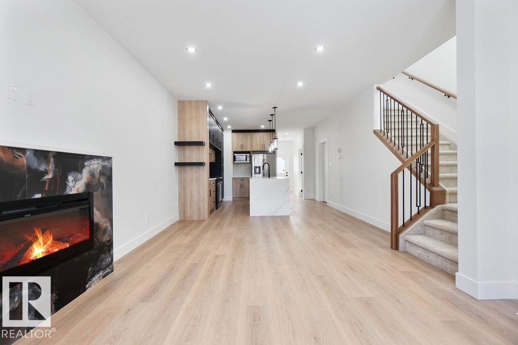 Living area featuring light wood flooring, a fireplace with a dark marble-look surround, recessed lighting, and a staircase with wood and black metal railings - 12307 91 St Nw, Edmonton, AB - Indoor With Fireplace