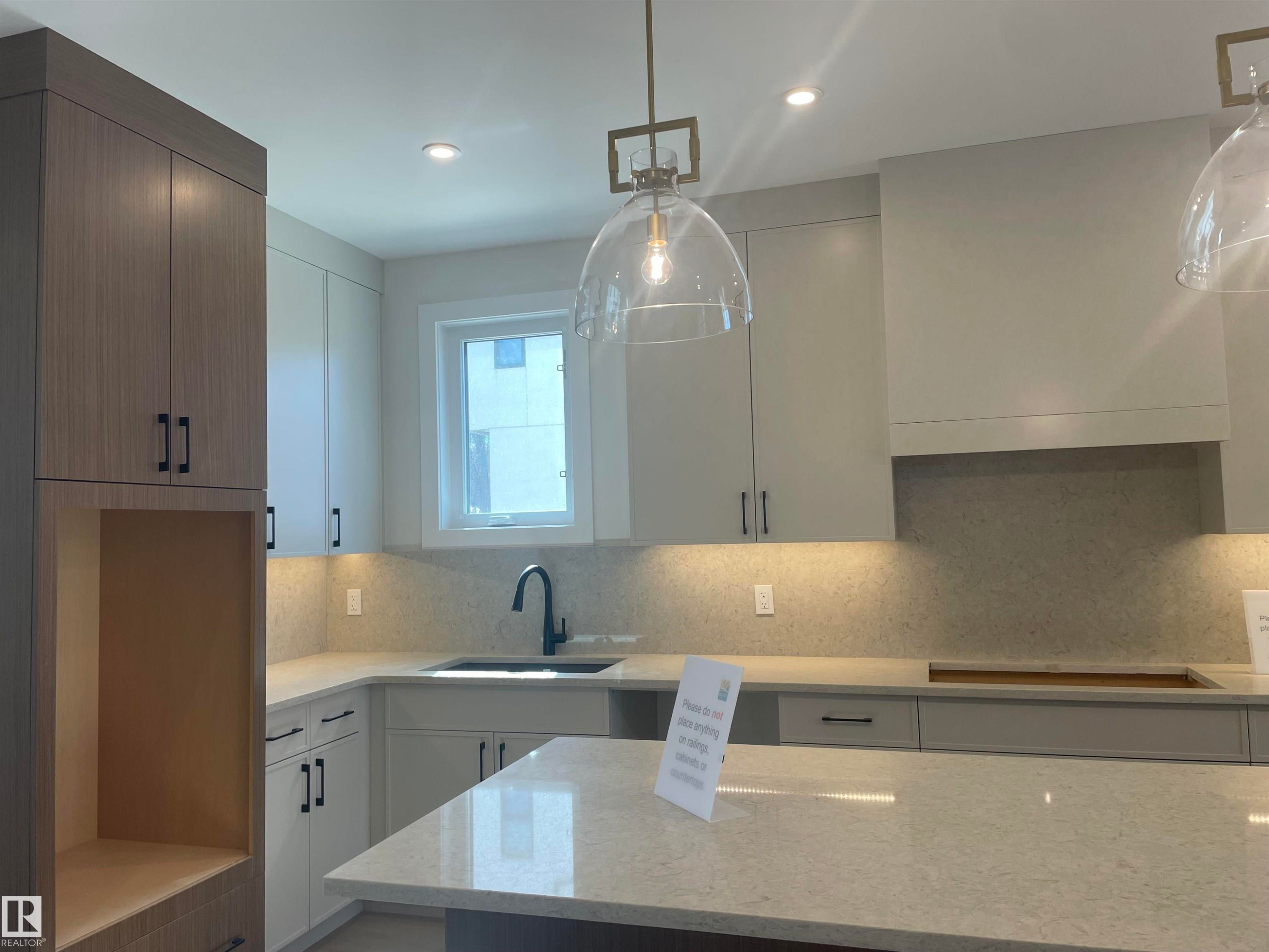 Contemporary kitchen featuring a large island with a light-toned countertop, a built-in sink with a black faucet, recessed lighting, and pendant fixtures - 14344 92A Avenue, Edmonton, AB - Indoor Photo Showing Kitchen With Upgraded Kitchen