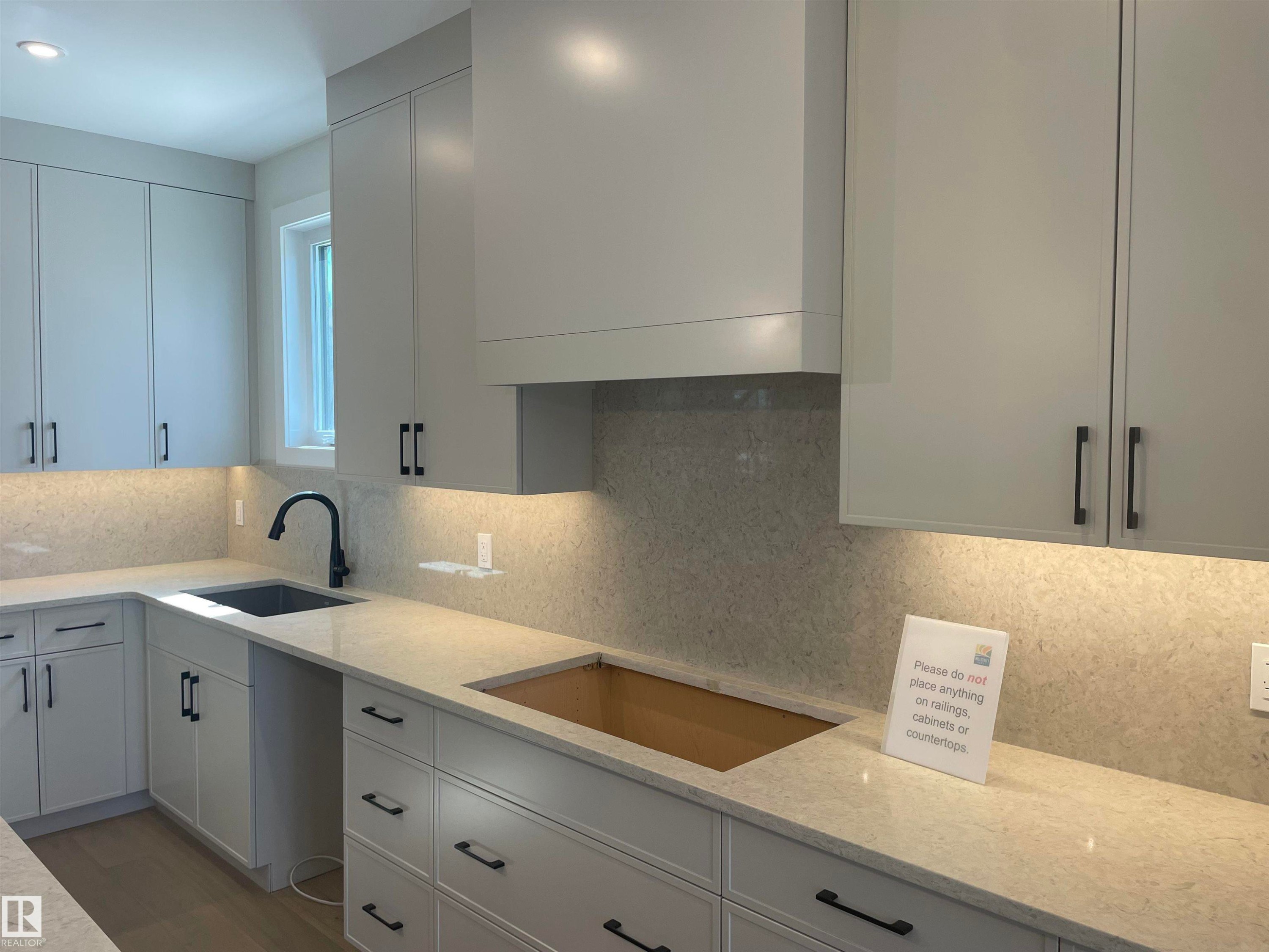 Contemporary kitchen featuring light gray cabinetry with black hardware, a black single-basin sink with a matte black faucet, and light-toned countertops extending as a full backsplash - 14344 92A Avenue, Edmonton, AB - Indoor Photo Showing Kitchen