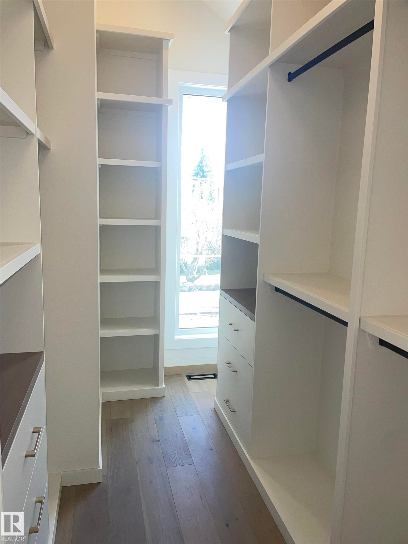 Custom-built closet system featuring wood-finish flooring, white cabinetry, built-in shelving, drawers with brushed nickel hardware, and hanging rods - 14344 92A Avenue, Edmonton, AB - Indoor With Storage