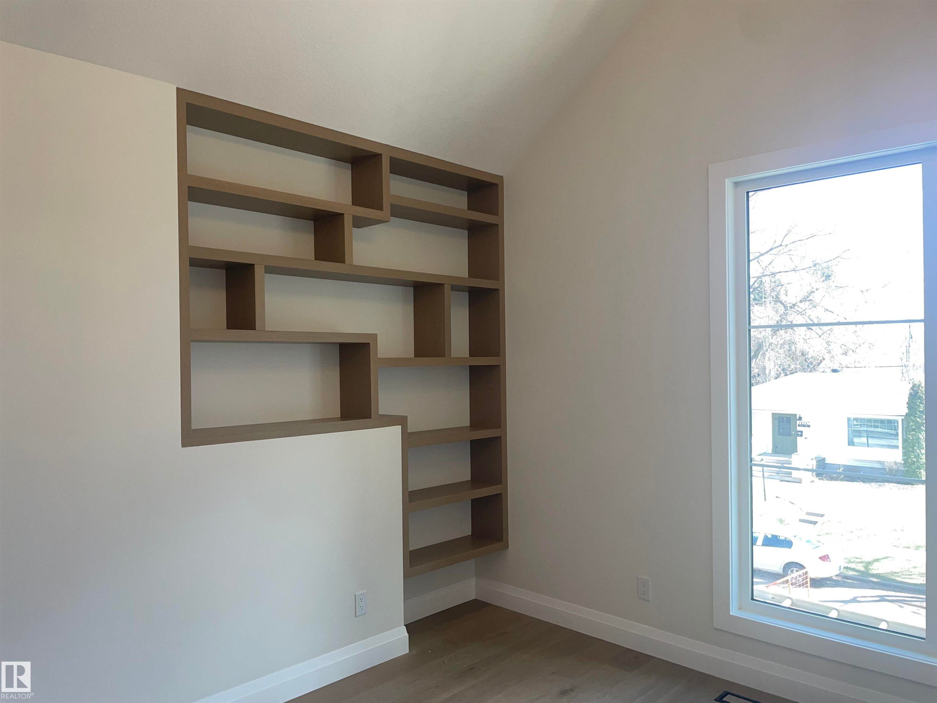 Built-in shelving unit with varied cubby sizes, natural light from a large window, light-toned wood-finish flooring, white baseboards, and a vaulted ceiling - 14344 92A Avenue, Edmonton, AB - Indoor