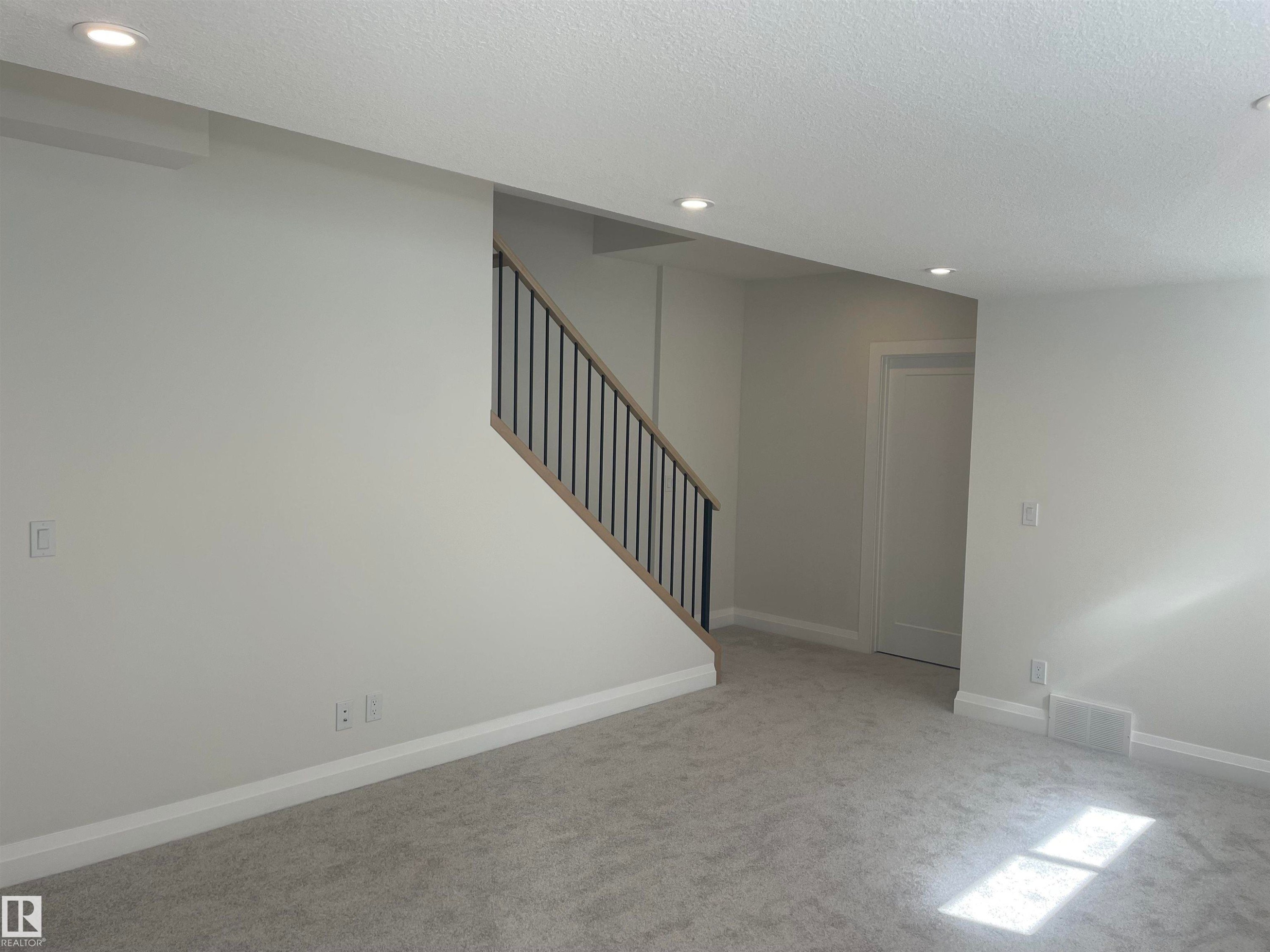 Carpeted room featuring a contemporary staircase with wood-finish handrail and black metal balusters - 14344 92A Avenue, Edmonton, AB - Indoor Photo Showing Other Room