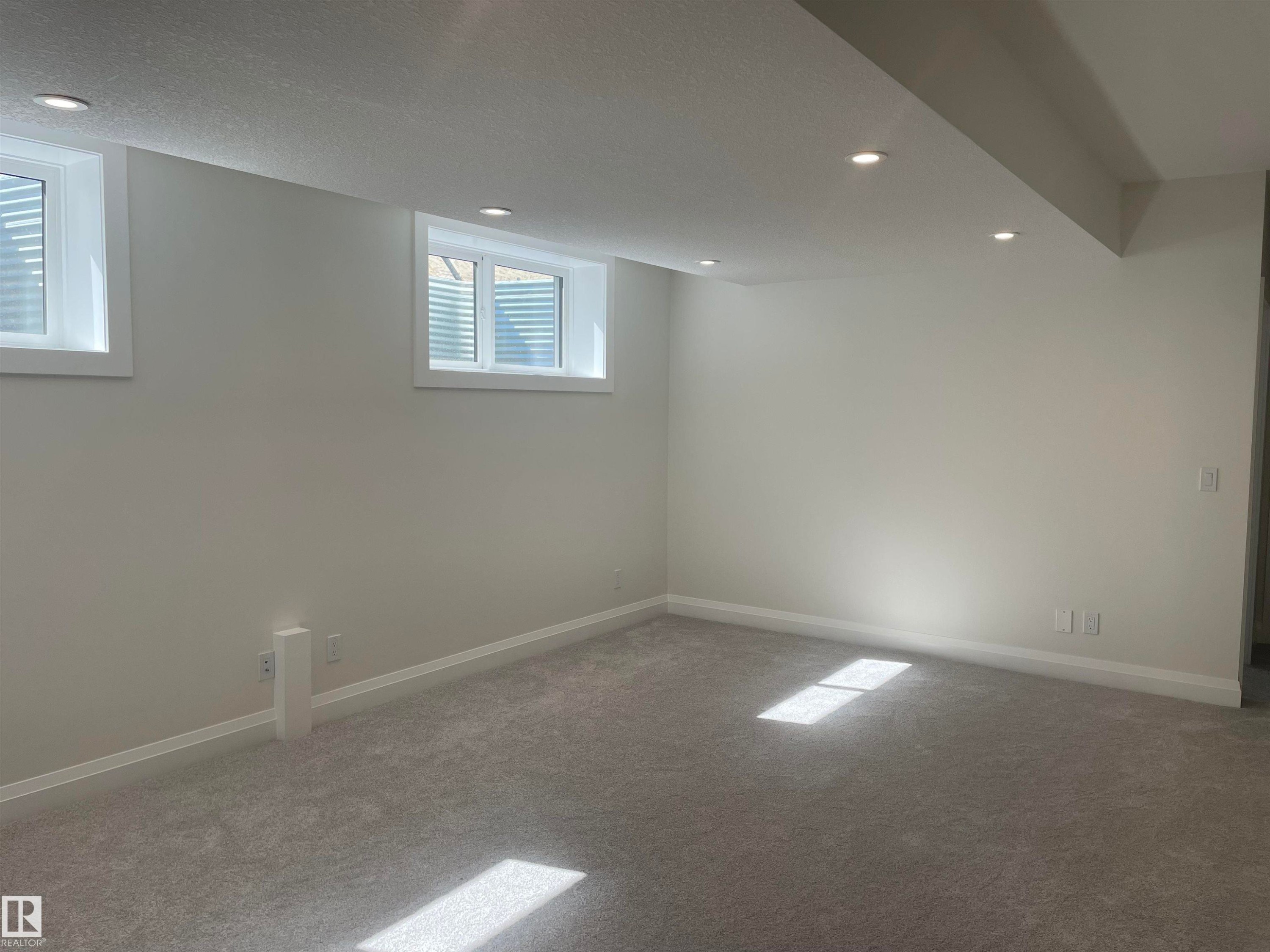 Spacious room featuring light gray carpeting, recessed ceiling lighting, two egress windows, and painted baseboards - 14344 92A Avenue, Edmonton, AB - Indoor Photo Showing Other Room