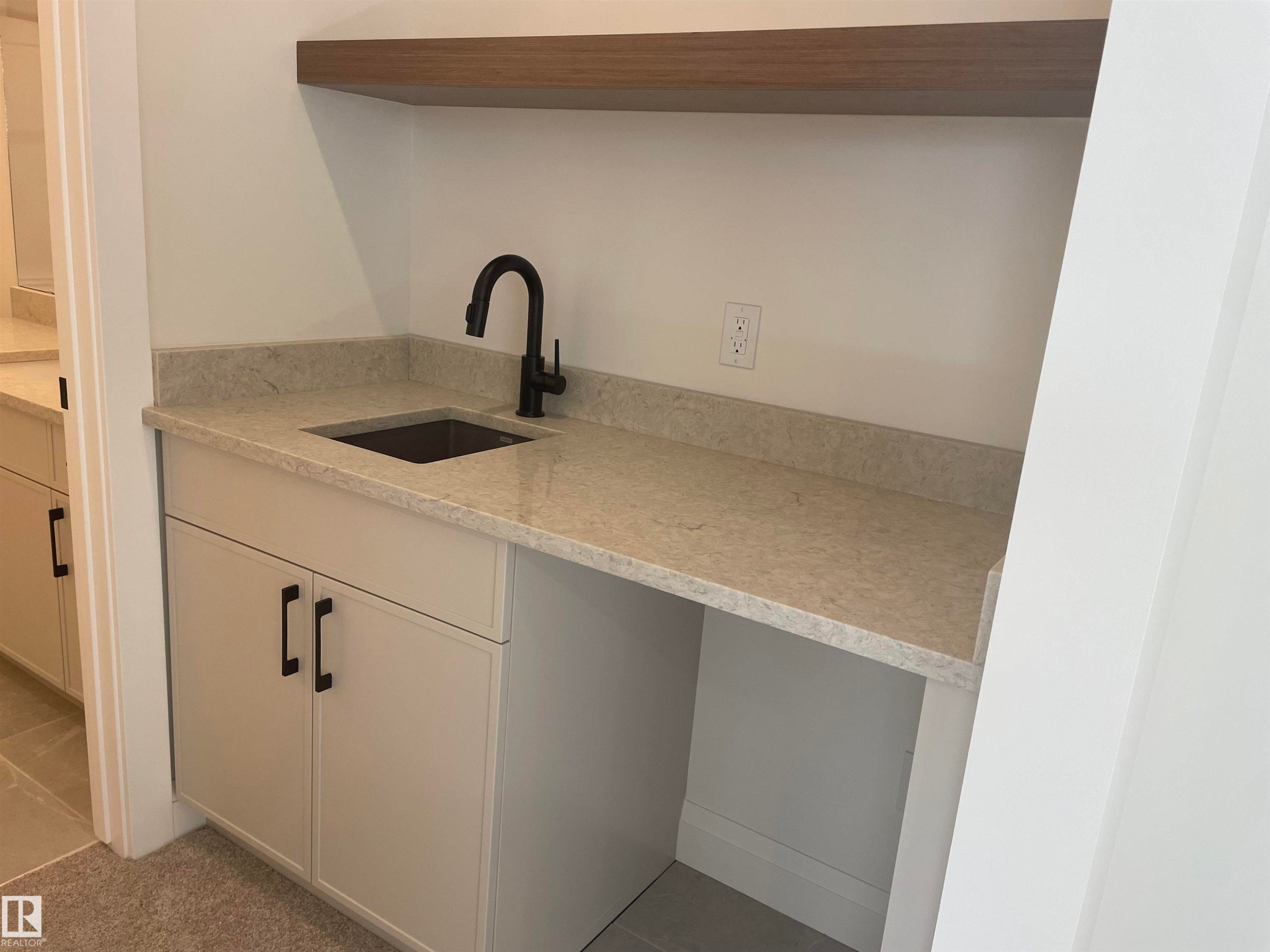 Integrated wet bar featuring a matte black faucet, dark basin sink, and light-toned stone countertop with matching backsplash - 14344 92A Avenue, Edmonton, AB - Indoor