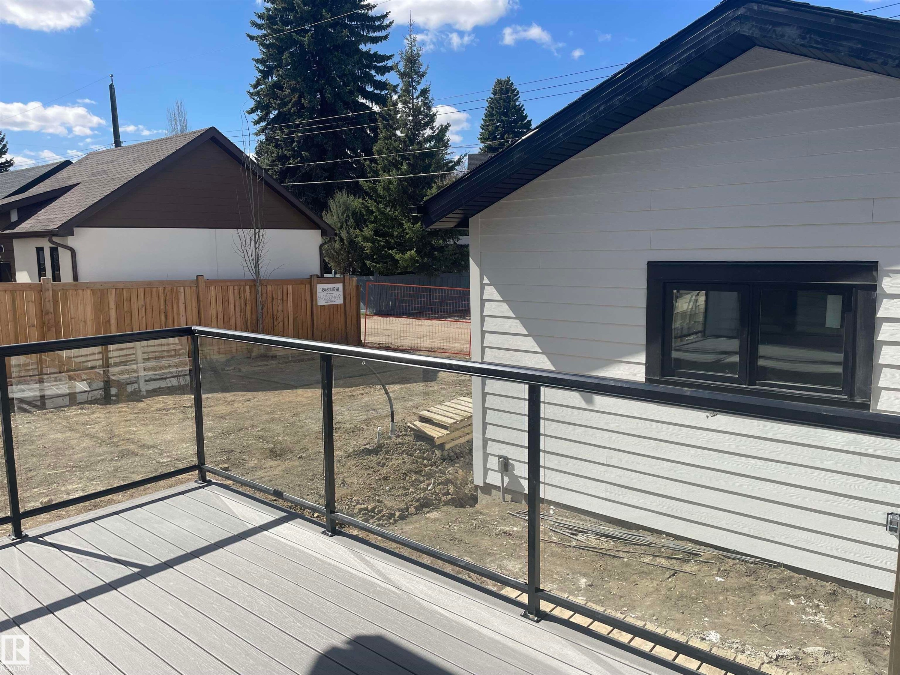 Rear exterior featuring white horizontal siding, black trim window, black soffit, and a gray composite deck with glass panel railing - 14344 92A Avenue, Edmonton, AB - Outdoor With Exterior