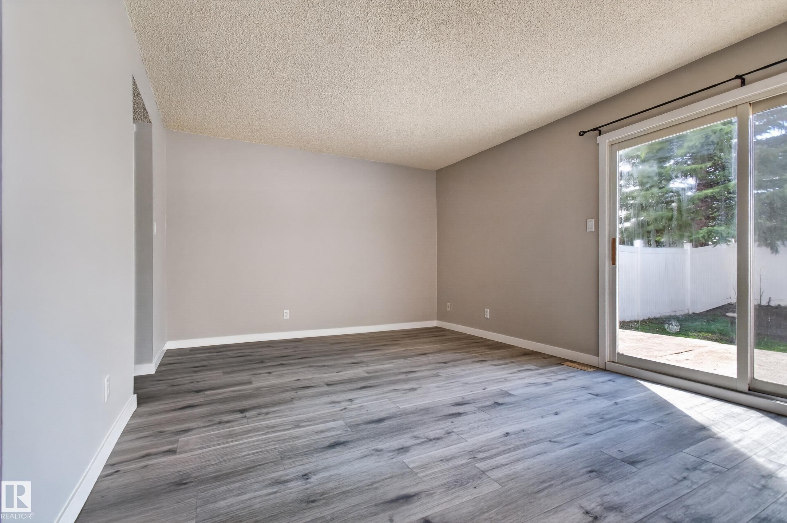 Spacious interior featuring wood-finish flooring, neutral wall tones, and a sliding glass door providing exterior access - 18 Lakewood Village, Edmonton, AB - Indoor Photo Showing Other Room
