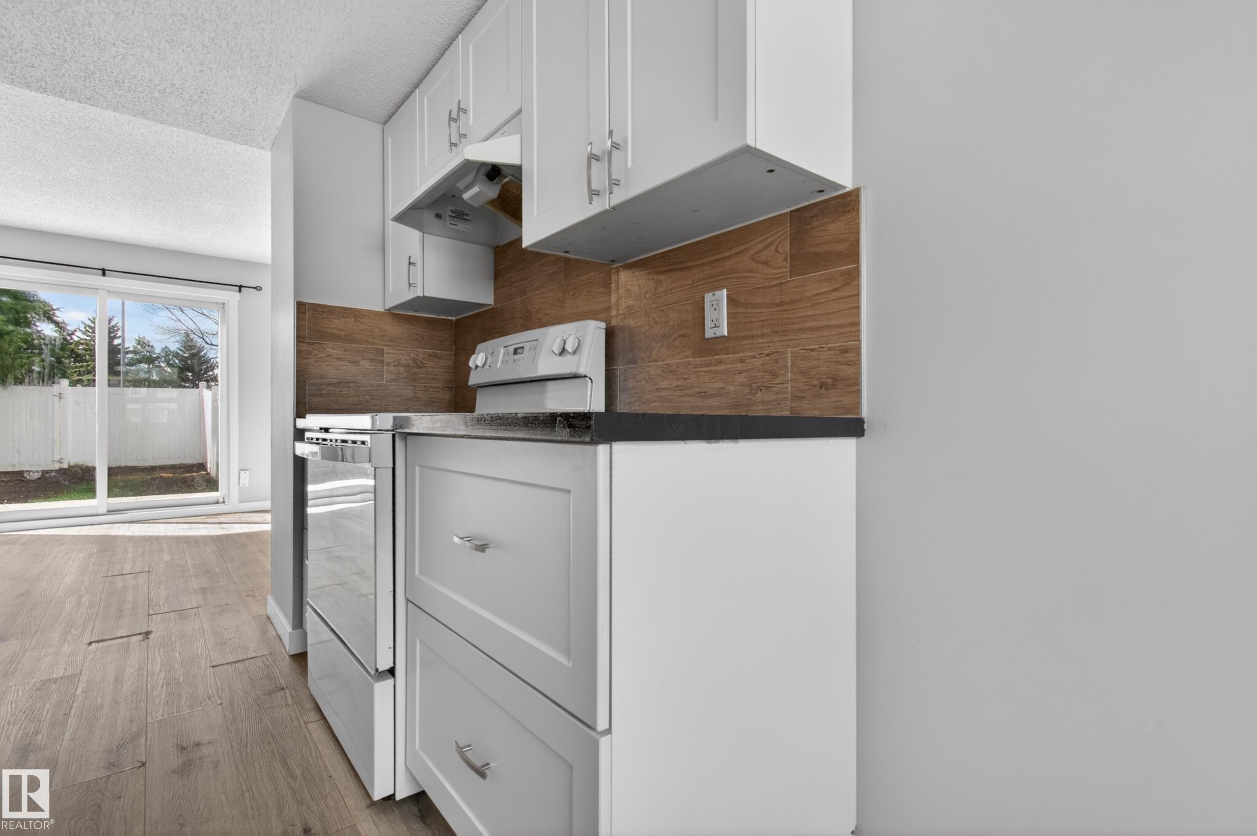Kitchen featuring white upper and lower cabinetry, dark countertops, a stainless steel range, and a wood-finish tile backsplash - 18 Lakewood Village, Edmonton, AB - Indoor Photo Showing Kitchen