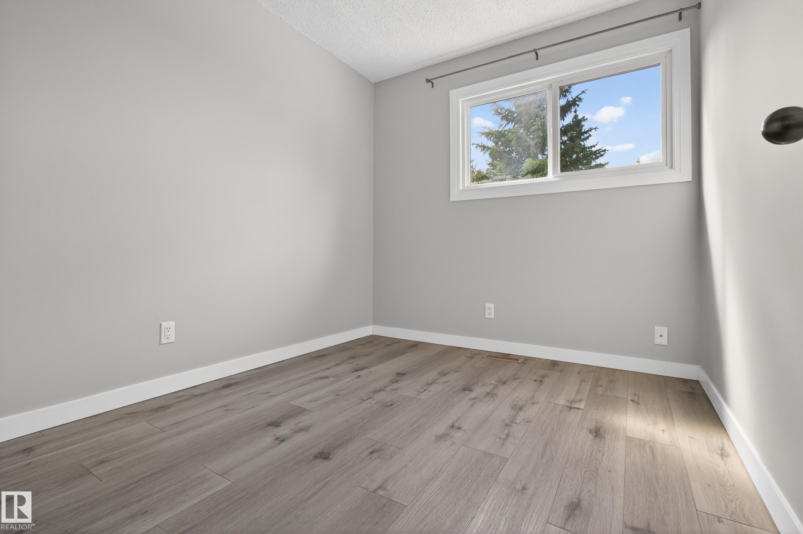 Interior room featuring wood-finish flooring, light grey painted walls, white baseboards, and a window with white trim - 18 Lakewood Village, Edmonton, AB - Indoor Photo Showing Other Room