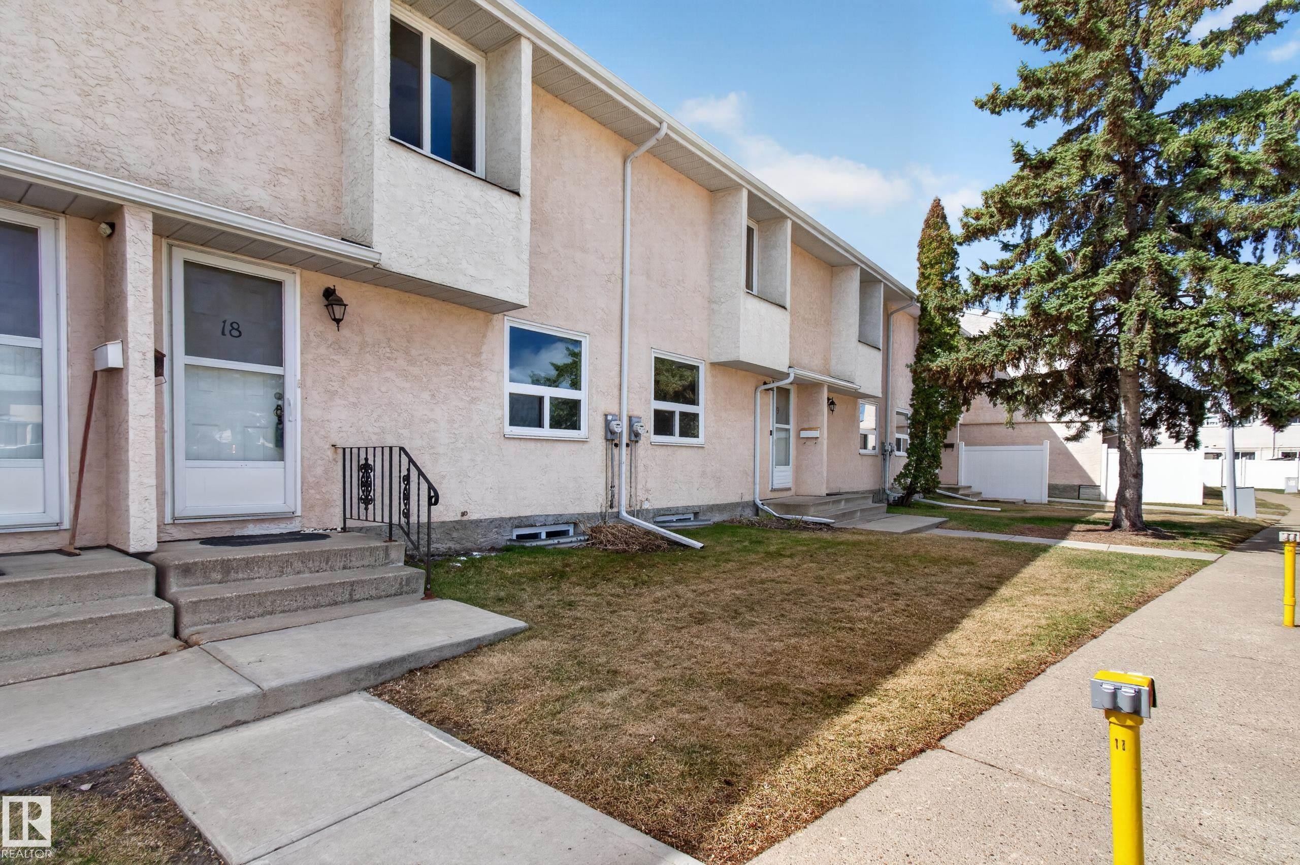 Multi-level stucco exterior featuring white-framed windows, a concrete walkway, and a landscaped front yard with a mature evergreen - 18 Lakewood Village, Edmonton, AB - Outdoor