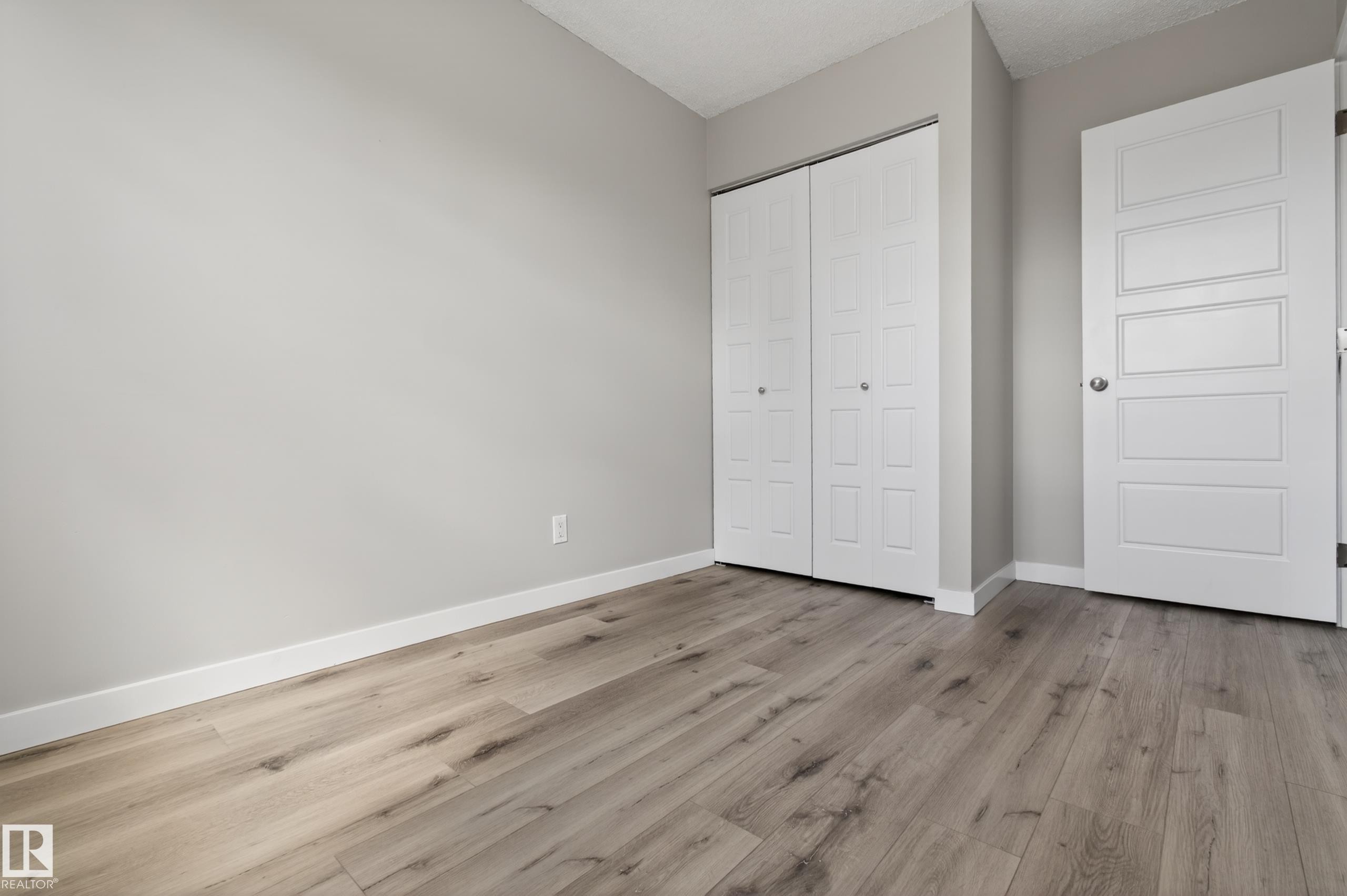 Light wood-finish flooring complements the neutral wall color in this room, featuring a white bi-fold closet door and a paneled interior door with a chrome knob - 18 Lakewood Village, Edmonton, AB - Indoor Photo Showing Other Room